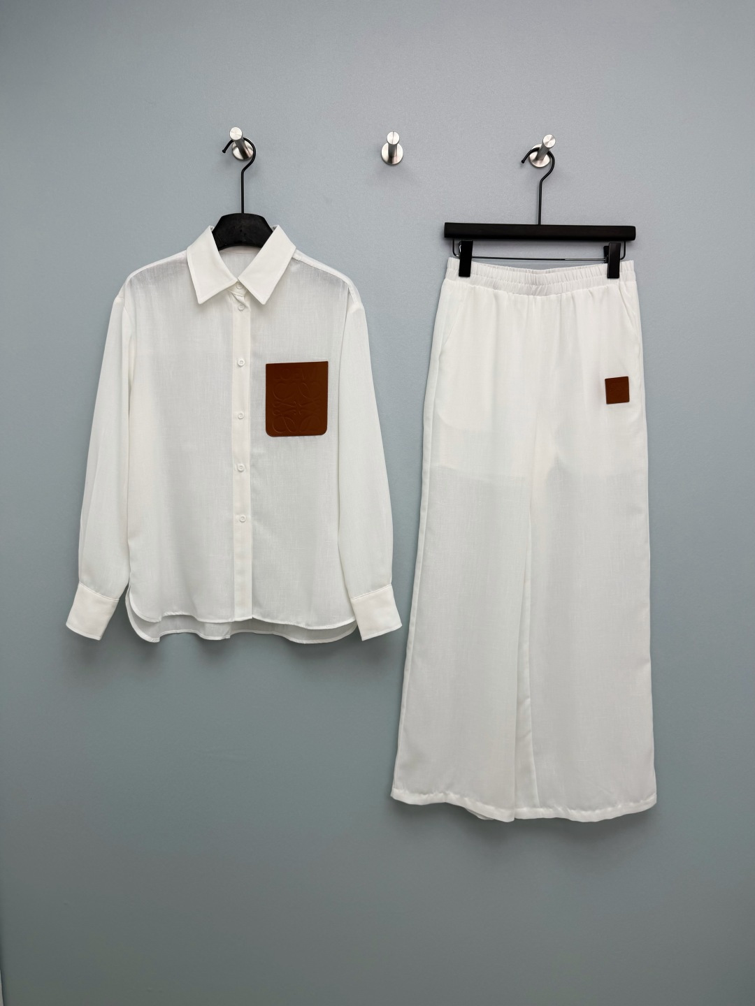 NO:780238,LOEW*26 new white shirt wide leg pants suit  The top has a classic lapel single-breasted design and a curved hem at the front, making it more casual. The left chest is embellished with the iconic brown embossed leather pocket, embossed with LOEW* brand letters and the Anagram four-leaf logo, which is the design soul of the whole set. Wide-leg pants  The elastic waist design is very tolerant to the figure; the wide-legged version of the same fabric is draped, visually elongating the legs; the trousers are embellished with small leather labels of the same series, echoing the shirt design, and the whole set feels full. This white shirt wide-leg trousers suit really welds the sense of relaxation and high-end  The fabric is extremely breathable, so you won’t feel sweaty when wearing it in summer. The slightly translucent texture comes with a cooling filter~Single color size 3 SML, Loewe-clothing, loewe, loewe, shirts,19860909LOEW*26新款白色衬衫阔腿裤套装 上衣经典翻领单排扣设计,前襟做弧形下摆,更显随性；左胸点缀标志性棕色压纹皮革口袋,压印LOEW*品牌字母与Anagram四叶logo,是整套的设计灵魂.阔腿裤松紧腰设计,对身材包容度极高；同面料垂感阔腿版型,视觉拉长腿型；裤身同系列小皮标点缀,呼应衬衫设计,整套感拉满.这套白衬衫阔腿裤套装真的把松弛感和高级感焊死了 面料巨透气,夏天穿完全不闷汗,微透的肌理感自带清冷滤镜~单色3码SML,罗意威-服装,loewe,loewe,shirts,,Women's clothing