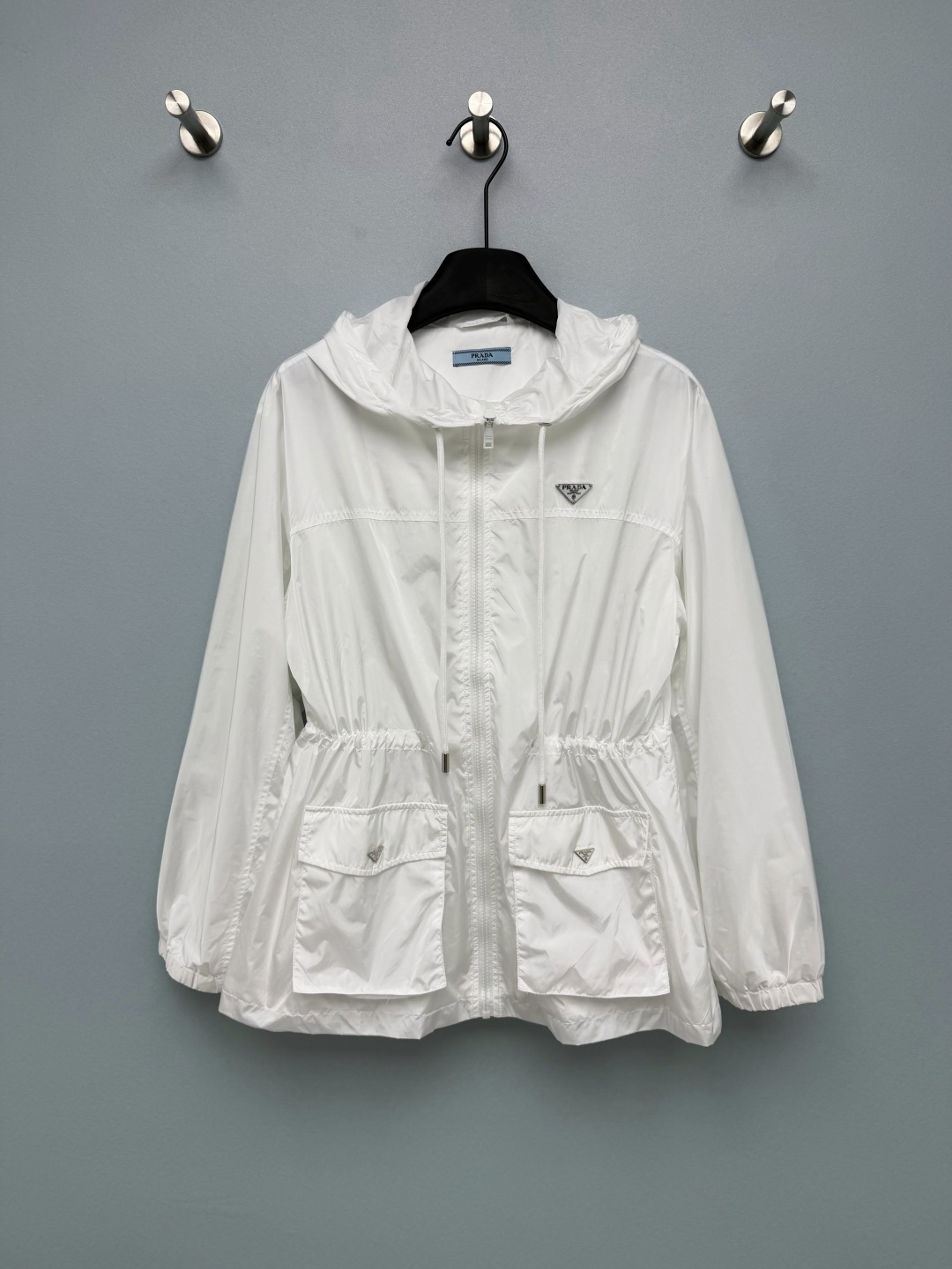 NO:828023,Prad*26 new style waist drawstring hooded sun protection jacket. Made of high-count nylon fabric, it has a light drape feeling, is light, breathable and not stuffy. The hooded design has a casual feel and can modify the face shape; the waist drawstring can be adjusted freely to easily create a high waistline.  The triangular metal logo on the chest and pocket is low-key and has its own brand recognition, which instantly enhances the overall sense of sophistication. The white color is refreshing and clean, and comes with a summer soft light filter. When paired with a light-colored inner layer, it looks super energetic; black is calm and slimming, and paired with a dark inner layer, it is neat and high-end!  2 colors and 3 codes SML, Prada-clothing, prada, prada, jackets & coats, hats,19860909Prad*26新款腰抽绳收腰连帽防晒外套 采用高支尼龙面料,自带轻盈垂坠感,轻薄透气不闷热 连帽设计自带休闲感,同时能修饰脸型；腰部抽绳可自由调节,轻松打造高腰线 胸口和口袋上的三角金属标,低调又自带品牌辨识度,瞬间提升整体精致感.白色清爽干净,自带夏日柔光滤镜,搭配浅色系内搭超显元气；黑色沉稳显瘦,搭配深色内搭利落又高级！2色3码SML,普拉达-服装,prada,prada,jackets & coats,hats,,Women's clothing