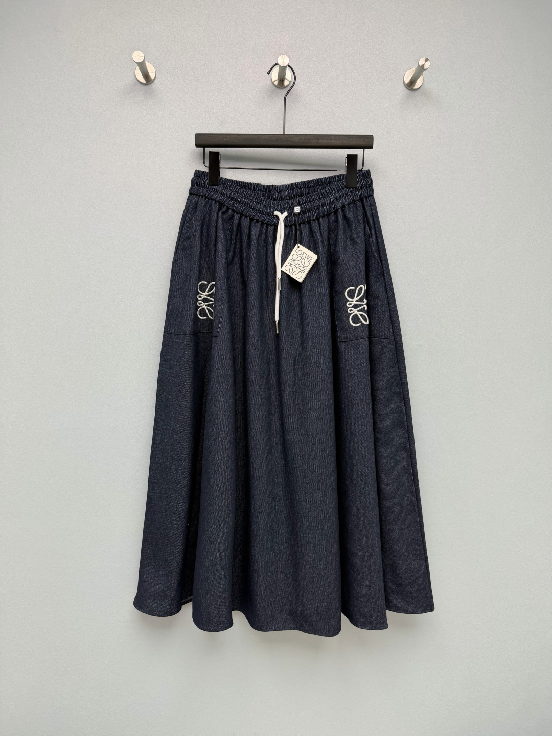 NO:855285,LOEW*26's new denim-textured A-line skirt uses the brand's iconic Anagram embroidery as the design highlight. Navy blue denim fabric with white embroidery is low-key and recognizable, with a relaxed Spanish aesthetic atmosphere. The high-waisted elastic drawstring waistband does not tighten the belly and optimizes the waist and abdomen lines; the large loose A-line skirt has a strong drape, which can easily hide the flesh of the legs and can also lighten the pear-shaped figure.  It is easy to control; the pockets on both sides are embroidered with Anagram, which is full of details and has both practicality and design. It is made of cotton and linen blended fabric with denim texture, which is dry and skin-friendly. The upper body is breathable and comfortable, has a good drape and is not easy to wrinkle and deform. It has a natural texture and will not be stuffy at all in summer. Monochrome 4-code SMLXL, Loewe-clothing, loewe, loewe, skirts,19860909LOEW*26新款牛仔质感A字半裙,采用品牌标志性的Anagram刺绣为设计亮点,藏青色牛仔面料搭配白色刺绣,低调又充满辨识度,自带松弛的西班牙式美学氛围.高腰松紧抽绳腰头,不勒肚子还能优化腰腹线条；宽松A字大裙摆,垂坠感超强,轻松藏住腿部肉肉,梨形身材也能轻松驾驭；两侧口袋带有Anagram刺绣,细节感拉满,实用性与设计感兼具.采用牛仔质感的棉麻混纺面料,触感干爽亲肤,上身透气舒适,垂坠感好且不易起皱变形,自带天然肌理感,夏天穿也完全不会闷热.单色4码SMLXL,罗意威-服装,loewe,loewe,skirts,,Women's clothing