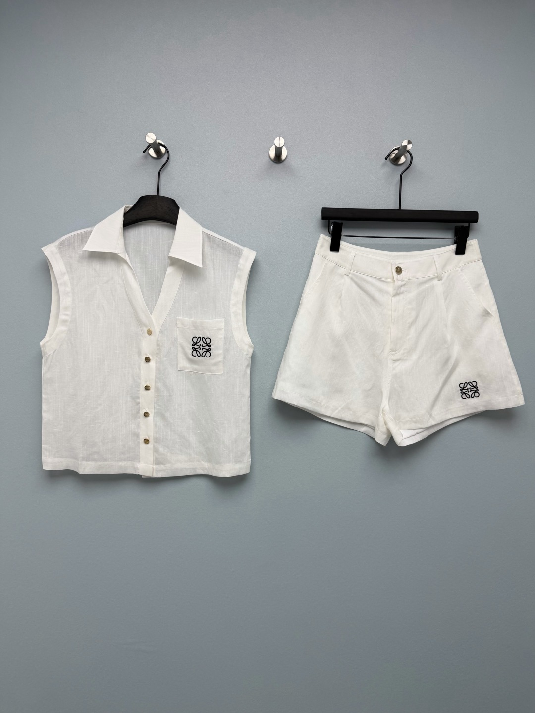 NO:855303,LOEW*26's new linen blend suit features the brand's iconic Anagram embroidery as the design highlight. It is available in black and white. It is simple and recognizable, with a low-key sense of luxury. The upper body can easily achieve the relaxed and elegant Spanish aesthetics. None  The sleeveless shirt + high-waisted shorts are a lazy fairy version. The lapel V-neck design exposes the delicate collarbone. The single row of metal buttons adds a sense of sophistication. The chest pocket has Anagram embroidery, which is full of details. The loose straight version does not flatter the figure and hides the flesh.  The high-waisted design of the shorts optimizes the waist and abdomen lines, and the middle front pleat design modifies the crotch line. The A-line version hides the flesh of the legs, and the Anagram embroidery on the trousers echoes the top. The overall shape is very complete. Made of breathable linen blended fabric, it has a natural texture. The upper body is dry and breathable, has a good drape and is not easy to wrinkle and deform. It will not be stuffy at all in summer, and has a lazy and relaxed atmosphere!  2 colors and 3 codes SML, Loewe-clothing, loewe, loewe, shorts, shirts,19860909LOEW*26新款亚麻混纺套装,以品牌标志性的Anagram刺绣为设计亮点,黑白两色可选,简约又充满辨识度,自带低调的高级感,上身轻松拿捏松弛贵气的西班牙式美学.无袖衬衫+高腰短裤的懒人神仙版型,翻领V领设计,露出精致锁骨,单排金属纽扣增加精致感,胸前口袋带有Anagram刺绣,细节感拉满,宽松直筒版型不挑身材,藏肉效果拉满. 短裤高腰设计优化腰腹线条,前中褶裥设计修饰胯部线条,A字版型藏住腿部肉肉,裤脚的Anagram刺绣与上衣呼应,整体造型完整度超高.采用透气亚麻混纺面料,自带天然肌理感,上身干爽透气,垂坠感好且不易起皱变形,夏天穿也完全不会闷热,自带慵懒松弛的氛围感！2色3码SML,罗意威-服装,loewe,loewe,shorts,shirts,,Women's clothing