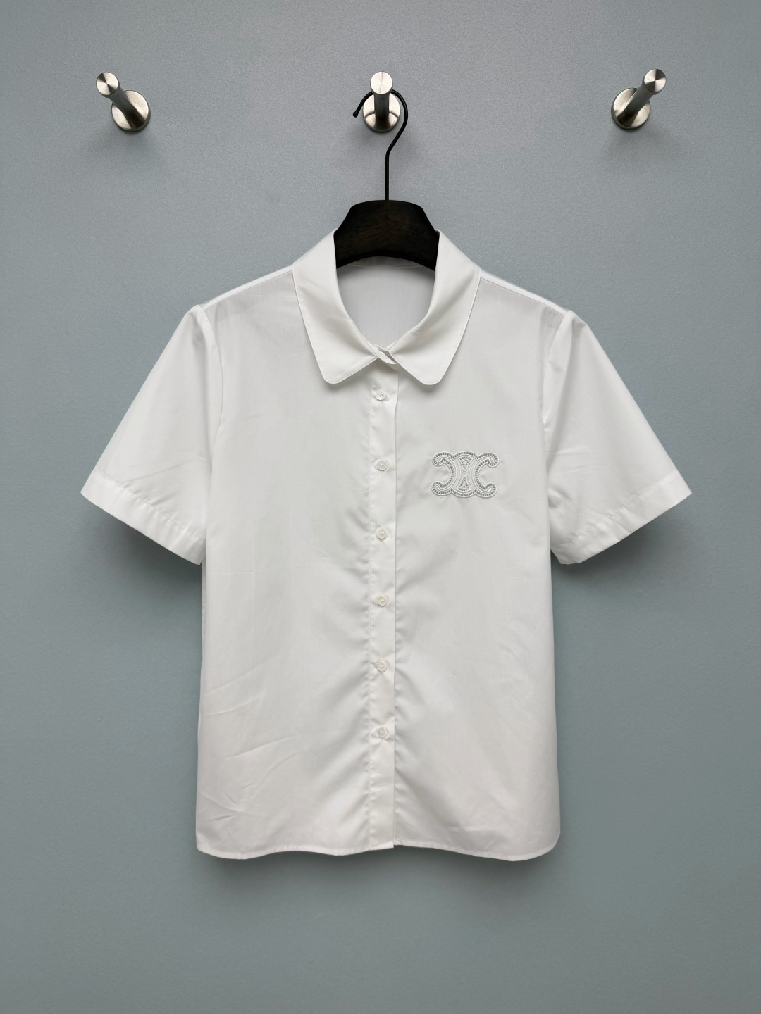 NO:861010,Celi*26 new Triomphe Arc de Triomphe series short-sleeved white shirt. The hollow embroidered Arc de Triomphe pattern on the left chest is the soul highlight of the whole piece. The delicate stitching creates a delicate hollow effect, which is low-key and recognizable, breaking the monotony of ordinary white shirts. The rounded baby collar has soft lines, weakening the seriousness of traditional shirts, adding a bit of gentle college temperament, paired with short-sleeved tailoring, refreshing and age-reducing. The gentle and capable feeling directly fills you!  Monochrome size 3 SMLB, Celine-clothing, celine, celine, shirts, T-shirt,19860909Celi*26新款Triomphe 凯旋门系列短袖白衬衫 左胸的镂空刺绣凯旋门图案是整件的灵魂亮点,细腻的针脚打造出精致的镂空效果,低调又有辨识度,打破了普通白衬衫的单调感.圆润的娃娃领线条柔和,弱化了传统衬衫的严肃感,增添了几分温柔学院气质,搭配短袖剪裁,清爽又减龄.温柔又干练的感觉直接拉满！单色3码SMLB,赛琳-服装,celine,celine,shirts,T-shirt,,Women's clothing
