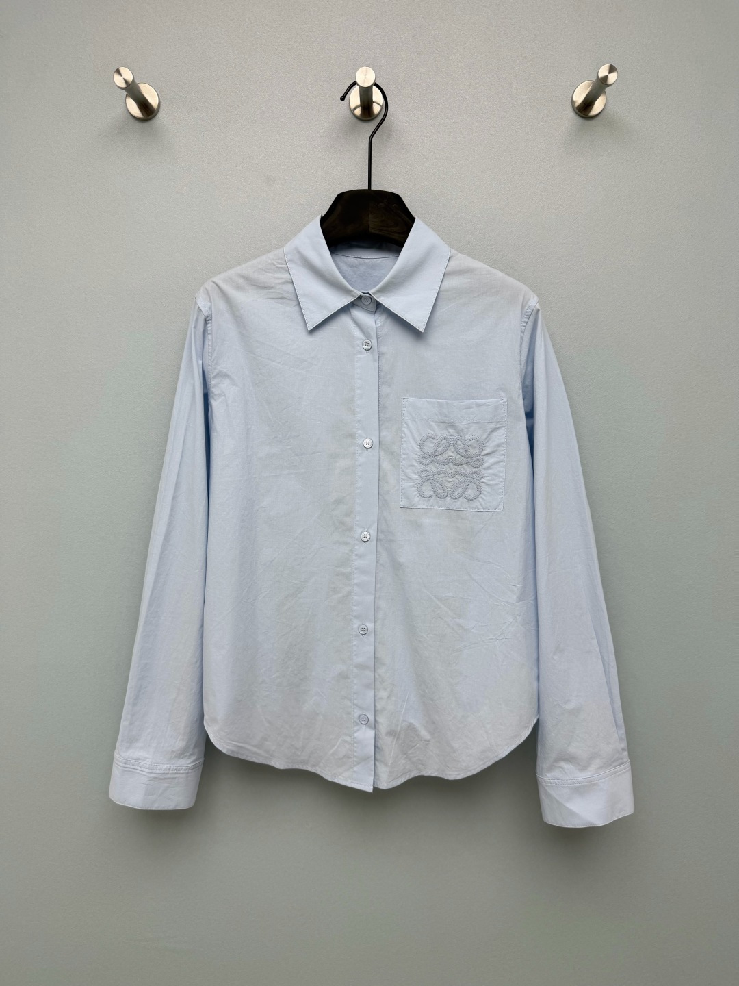 NO:864203,LOE*26 new style pocket embroidered back pleated light blue shirt  Classic small square lapel + full placket with buttons of the same color, neatly modifying the neck, neatly routed placket, simple and basic style for commuting. The left chest patch pocket uses thick line three-dimensional Anagram embroidery of the same color, the knot texture is full and three-dimensional, and the low-key dark pattern design  Highlights the brand's texture. The back piece is cut with multiple vertical pleats, loose and loose structure, modifying the back line, hiding the flesh and making it slimmer, and lifting the hands without restraint. The short arc hem of stonewashed cotton has a lazy wrinkle feeling, the upper body is soft and comfortable, and the refreshing light blue is super bright!  Single color code 3 SMLB,,loewe,shirts,19860909LOE*26新款口袋刺绣后打褶浅蓝色衬衫 经典小方翻领+全开襟同色纽扣,利落修饰脖颈,门襟走线工整,简约通勤基础版型.左胸贴袋处采用同色系粗线立体Anagram刺绣,绳结肌理饱满立体,低调暗纹设计凸显品牌质感.后片多道竖向活褶剪裁,宽松散摆结构,修饰后背线条,藏肉显瘦,抬手无束缚,短款圆弧下摆石磨水洗棉自带慵懒皱感,上身软糯舒服,清爽浅蓝超显气色！单色3码SMLB,,loewe,shirts,,Women's clothing