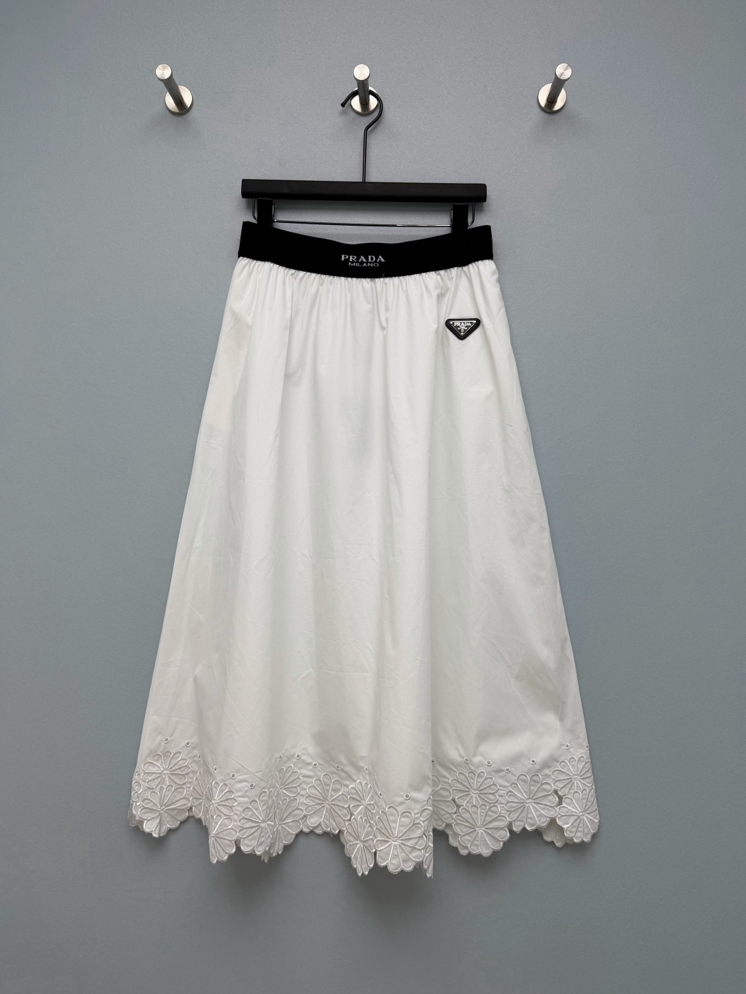 NO:944055,PRA* embroidered lace elastic waist A-line midi skirt  High count poplin cotton fabric, crisp and dry, with good drape, can support the fluffy silhouette of the skirt, breathable and easy to take care of. Black wide-brimmed elastic waist, webbing with printed logo, comfortable to put on and take off without restraint. Classic metal triangle logo badge on the side, brand  The brand is highly recognizable. The hem has a large area of three-dimensional flower embroidery with hollow lace, and the wavy irregular trimming is exquisite and romantic, neutralizing the neatness of the poplin fabric. The cotton umbrella skirt can be either salty or sweet, it is difficult to choose between black and white, and the embroidered lace on the hem is amazing!  Two-color code 4 SMLXL,Prada-clothing,prada,prada,skirts,19860909PRA*刺绣花边松紧腰A字中长半裙 高支府绸棉质面料,挺括干爽,拥有良好垂感,能够撑起裙身蓬松廓形,透气好打理.黑色宽边松紧腰,织带有印刷标识,穿脱舒适无束缚.侧边经典金属三角标徽章,品牌辨识度拉满.下摆大面积立体花朵刺绣镂空花边,波浪不规则裁边,精致浪漫,中和府绸面料的利落感.可盐可甜的棉质伞裙,黑白双色很难抉择,下摆刺绣花边太绝了！ 双色4码 SMLXL,普拉达-服装,prada,prada,skirts,,Women's clothing