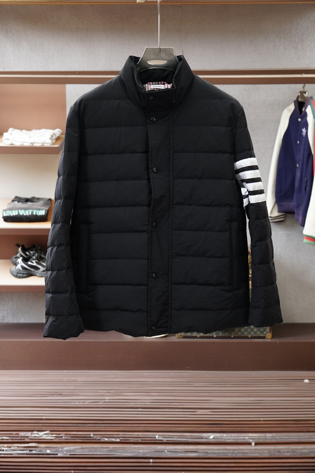 NO:661618,Thom Browne 2025FW new autumn and winter product. Classic four-bar jacket down jacket, which combines minimalist tones with luxury details. Fabric and warmth. Made of matte black fine fabric, with low-key texture; filled with 90 white goose down inside, with high fill power and strong warmth. The upper body is light and not bloated. It can lock in temperature without feeling heavy when worn in cold weather. Design details  The logo is ingenious. The iconic four white bars on the left arm + the red, white and black webbing logo on the back of the neck are the iconic symbols of TB, which are low-key and highly recognizable; the letter logo engraved on the buttons hides the brand details in the square inches; the practical structure of the stand-up collar + hidden buckle + zipper double closure design can not only tighten the cold wind, but also ensure the convenience of putting on and taking off; the hidden pocket on the back combines storage and simple vision; style adaptation  The minimalist black tone can be worn with trousers of the same brand for a yuppie commuting style, or with jeans and sweatpants for a relaxed street feel. It is a 'universal item' that combines warmth and style in the cold season. ……………………………………………………………… SizeM-XXL,,thom browne,jackets & coats,down jacket, 19860909Thom Browne 汤姆·布朗 2025FW秋冬新品 经典款四杠夹克羽绒服,把极简调性与细节奢感揉得恰到好处 面料与保暖 采用哑光黑细密面料,自带低调质感；内里填充90白鹅绒,蓬松度高、保暖性强,上身轻便不臃肿,冷天穿既锁温又无负重感. 设计细节 标识巧思左臂标志性四道白杠+后颈红白黑织带标,是TB的标志性符号,低调中自带高辨识度；纽扣上的字母标识刻印,把品牌细节藏在方寸之间； 实用结构立领+暗扣+拉链双重闭合设计,既能收紧寒风,又保证了穿脱便捷性；后背隐藏式口袋兼顾收纳与简约视觉； 风格适配 极简黑的调性,既能搭同品牌西裤走雅痞通勤风,也能配牛仔、运动裤穿出松弛的街头感,是冷季里兼具保暖与格调的“万能单品”. …………………………………………………… SizeM-XXL,,thom browne,jackets & coats,down jacket, ,Men's clothing