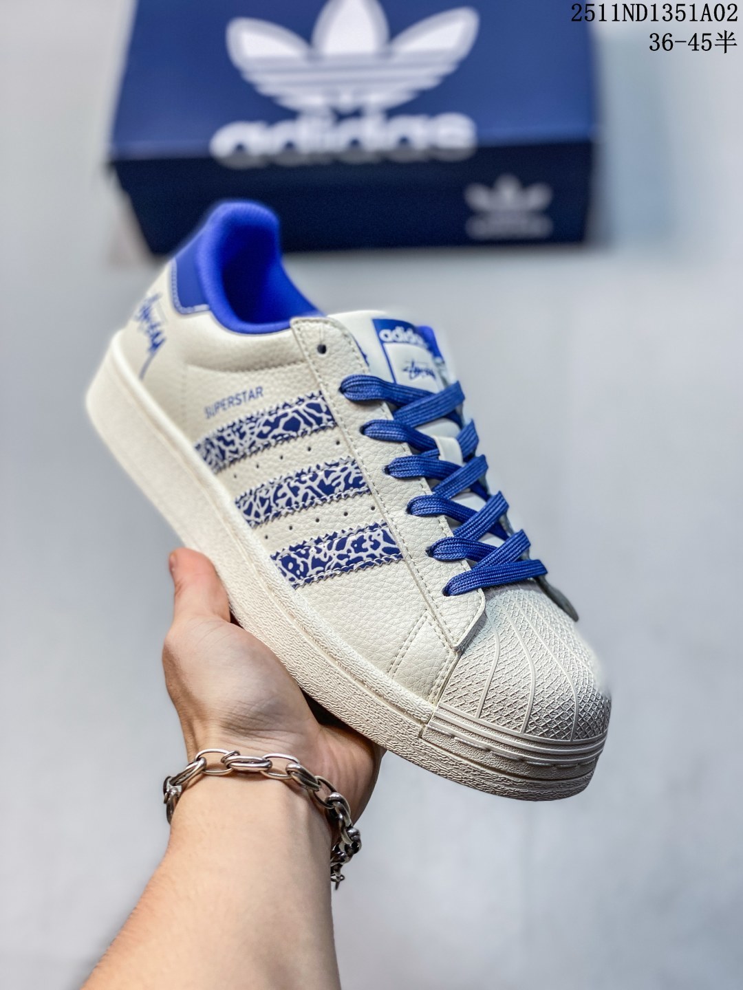 公司级 高端定制adidas Superstar 斯图西联名-白蓝 延续 Adidas 标志性贝壳头,以米白为主调的鞋身,宛如复古画报的底色,质感皮质细腻又挺括,复刻着半个世纪前的经典廓形.三道杠缀满蓝白涂鸦纹理,是 Stüssy 标志性的艺术表达;鞋舌、后跟的深海蓝撞色,像街头潮人随性搭的配饰,还有专属金属三叶草挂饰 高端定制 低帮休闲板鞋 定制鞋盒 大厂品质出货 超高清洁度 皮料切割干净无任何毛边 细节完美 货号:XG0009 ND1351A02