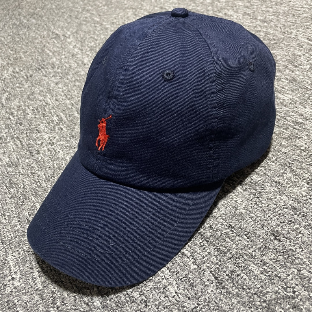 S# Ralph Lauren 拉夫劳伦 小马标 鸭舌帽 藏青/卡其 真正原版购回开发打版 高端零售专供 品质保证 100%放心出街 均码（52CM-62CM) 增礼佳品 ！附赠全套包装及定制手提袋 材质与工艺细节 主要材质 帽身： 采用高品质棉质帆（Cotton Twill）帆布材质紧密、硬挺有型，质感高级且耐磨 帽檐： 内部有内衬，采用轻质的聚合物板，使其能够轻松弯曲定形且不易折断，恢复性好 扣具： 金属按扣和棉质调节带，金属扣质感厚重，表面打磨光滑，刻有品牌Logo“Polo” 内里： 与头部接触的部分通常采用舒适吸汗的棉质或缎面材质，车线工整，不会有粗糙的线头 核心工艺细节： 刺绣工艺：清晰立体，标志性的Polo Player（马球手）Logo 或RL字母Logo 是核心，正品刺绣非常精致，针脚密集、均匀、饱满，图案边缘清晰锐利，无多余线头 色彩精准： 马球手的马鞍、马缰、球杆、衣服等不同部分的颜色区分清晰，即使是很小的细节也不会糊成一团 结构剪裁：帽身由6片面料拼接而成，拼接处的车线非常工整均匀，走线平直，弧度自然 定形工艺： 帽檐的弧度经过精心设计，既经典又现代。帽冠的弧线饱满，佩戴起来头型好看 重要鉴定点（真伪辨别） 假货（Fake）通常在以下细节上露出马脚 Logo刺绣 – 最重要的鉴定点 大货💯： 马球手Logo栩栩如生 马球杆： 球杆清晰可见，与手臂有区分 马腿： 至少能看到2-3条马腿的轮廓，线条分明 马鞍和马缰： 细节清晰，不会绣成一坨 整体比例： 马球手的身材比例协调，动作自然 市场版本❌： 刺绣粗糙、稀疏、扁平，马球杆可能看不清，马腿糊在一起，整体看起来呆板、畸形，充满廉价感 ！ 内部标签（Oxford Label） 真品材质： 通常是柔软的牛津布，质感好 印刷： 字体清晰、干净、粗细均匀“Ralph Lauren”字样精致-选品中心