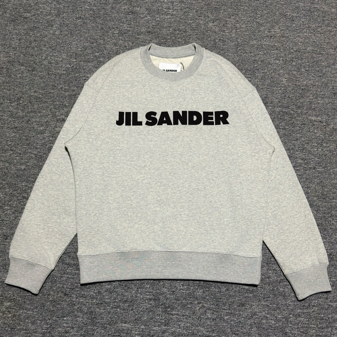 S# Jil Sander 吉尔桑德 大字母圆领卫衣 真正原版购回开发打版 高端零售专供 品质保证 100%放心出街 编号:29IEFF77 面料:21支精棉鱼鳞卫衣,460克,100%棉 罗纹:32支三股扁机罗纹,720克 独家定织定染高品质精梳棉面料,100%纯棉成分,大货面料手感绵柔,上身舒适透气,整体面料质感做到与原版品质相同! 原版底面鱼鳞毛圈,是偏“米黄色”的,面料需要经过一道特殊工艺处理 而市面很多版本,做出来的面料,毛圈底面是“纯白色”的,一眼假! 印花工艺:菲林开版 椭圆机“丝网印刷”工艺 独家订购进口特黑水性胶浆.胶浆材料渗透入面料,表面布纹清晰,不掉色,无胶感,拉开印花出现有“撕裂”条纹,透气性强.材料工艺均与原版一致 历经3次修改细节版带.对照原版印花图案,所有细节1:1还原,字体清晰简约,颜色深浅也与原版相同 对版1:1定做领标辅料,奢侈品的最高仪式——纯手工“挑纱手缝领标”,要求手缝师傅技术精湛,费时费力,工艺做法与原版相同 工匠手缝一件短袖,大概需要5-10分钟时间!非常麻烦! 挑纱手缝领标,是传统手工技艺与现代服装美学的结合,通过精细的“藏针”手法,在保证功能性的同时,提升衣物品质感.尽管效率不及机器生产,但其对细节的把控使其成为高端服饰的标志性工艺之一
