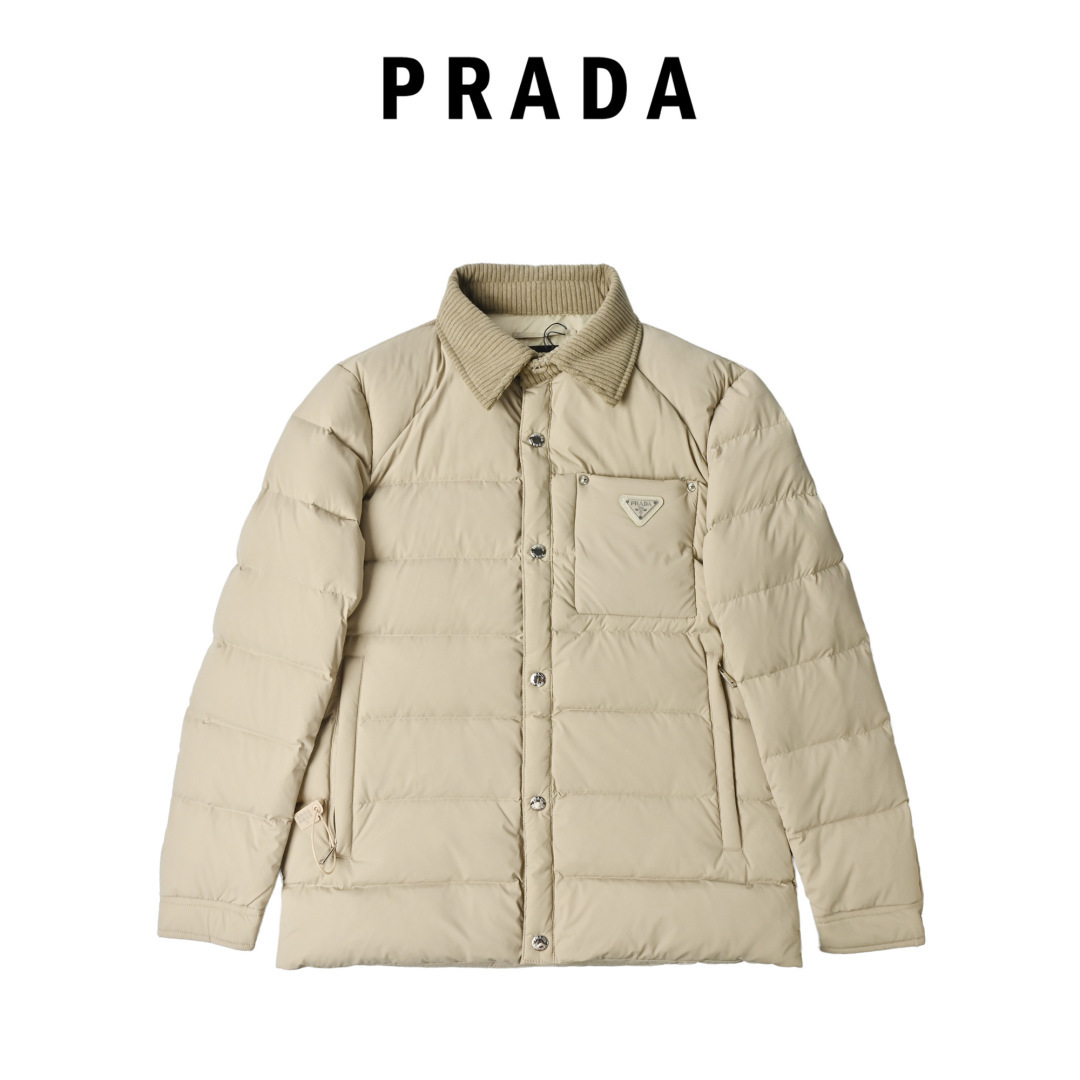 Prada/普拉达 本地自取 25FW 新款轻薄胸前刚标 立领男女同款羽绒服 这是一件Prada(普拉达)2025秋冬新款男士防风翻领羽绒服,具有以下特点: • 品牌与设计辨识度:胸前的珐琅涂层经典三角标口袋是Prada的标志性元素,灯芯绒翻领与羽绒衣身形成材质对比,展现品牌一贯的轻奢调性. • 面料与保暖性:采用客供进口的锦纶氨纶混纺面料,兼具防风拒水性能;内里填充90%白鹅绒,保暖且不显臃肿,实现“风度与温度并存”. • 细节工艺:配备客供定制的银色立体刻印Logo金属纽扣,细节处彰显高品位;休闲直筒剪裁,适配日常、休闲乃至部分正式场合的穿搭需求. • 风格定位:属于奢侈品牌的高定风格单品,融合了功能性与时尚设计,是追求简约摩登、低调奢感男士的优选.