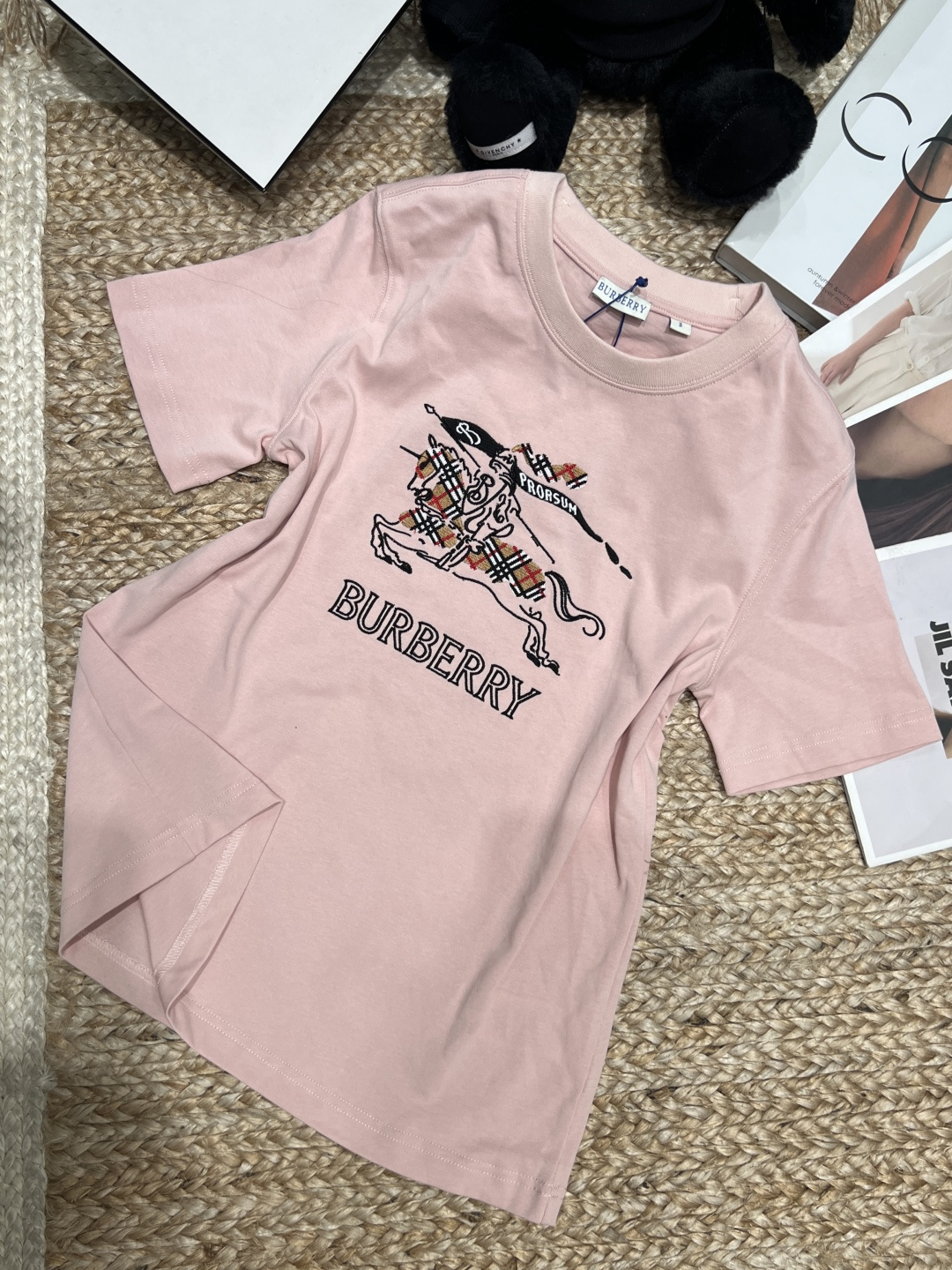 NO:830197,——Burber**——2026 SS sketch knight logo T-shirt, made of lightweight poplin cotton, comfortable and breathable to wear. The equestrian knight logo on the chest is embroidered with chain stitches, the sketch lines are super artistic, and the plaid details are low-key to show the brand's classics. The shape is neat, the shoulder design is available in white and pink, it is versatile and fashionable, and it is great whether worn alone or layered, and it is easy to create a British style look!  SML XL,Burberry-clothing,burberry,loro piana,tees,t-shirt,19860909——Burber**——2026年SS素描骑士徽标T恤,采用轻盈府绸棉,穿着舒适透气.胸前马术骑士徽标用链式缝线刺绣,素描线条感超有艺术气息,格纹细节低调展现品牌经典.版型利落,正肩设计,白色和粉色可选,百搭又时髦,无论单穿还是内搭都很出彩,轻松打造英伦风造型！SML XL,博柏利-服装,burberry,loro piana,tees，t-shirt,,Women's clothing