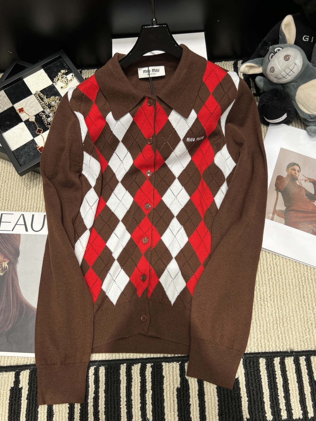 NO:958282,——Miu Mi*——2026 new autumn and winter diamond knitted cardigan made of wool blend material, soft and elastic, super comfortable to wear in autumn and winter!  The red, brown and white diamond pattern + lapel design is full of retro college style, reducing age and looking whiter. The front metal buttons have exquisite details, and the cuffs and hem are ribbed to modify the body shape and prevent it from deforming. Pair it with a skirt or trousers, and you can easily get a retro girly look!  Code numberSML,,miumiu,skirts,19860909——Miu Mi*——2026秋冬新款菱格针织开衫羊毛混纺材质,柔软有弹性,秋冬穿超舒服！红棕白菱格纹+翻领设计,复古学院风满满,减龄又显白.正面金属纽扣,细节精致,袖口和下摆罗纹收口,修饰身形不易变形.搭配半裙或长裤,复古少女感轻松get！码数SML,,miumiu,skirts,,Women's clothing