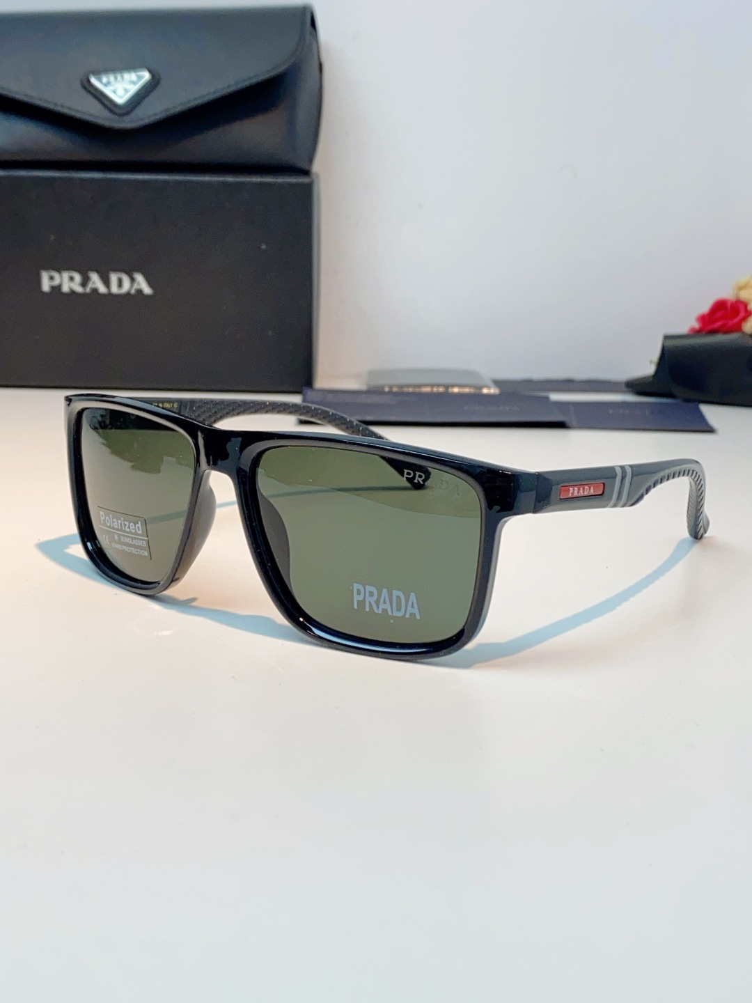 Prada普拉达 男士偏光太阳镜，经典方型镜框设计，哑光/亮面质感镜架搭配标志性红标，低调彰显品牌辨识度