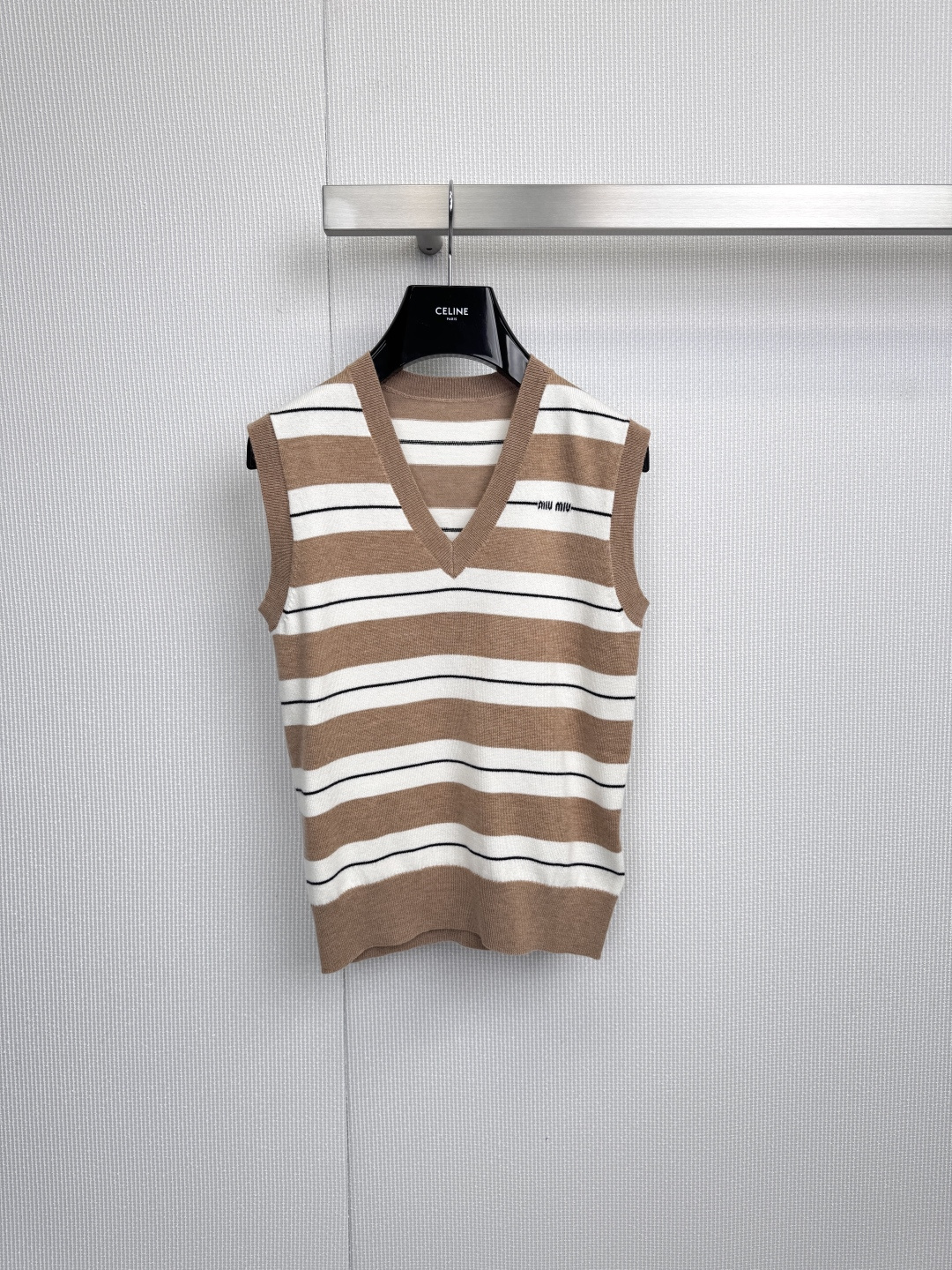 NO:590504,MiuMiu's new striped knitted vest has a retro college style and is the finishing touch for layering looks. It has brown and white stripes, which seem to bring the modern atmosphere of retro film to the body. This knitted vest has a neat V-neck design to unlock the possibility of layering. Whether it is worn with a white shirt to create a cute college feel, or with a black base shirt to highlight the rhythm of stripes, it can make the basic outfit instantly have a layered soul. The brand embroidery on the left chest quietly declares taste with delicate stitches, and the horizontal stripe texture  It collides with the cool luster of the metal hanger to create a wonderful tension. The soft knitted material retains the gentle touch of the skin, and the silhouette tailoring gives the body room to stretch - finding a delicate balance between restraint and freedom, from the hanging posture in the wardrobe  With a stunning transformation when the upper body is in shape, this vest is destined to be a magic weapon for styling in spring and autumn. It can accompany you to interpret the bookish style by the window of the cafe, or the playful and smart look when strolling on the street, hiding Miu Miu's rebellious girl's heart in the rhythm of stripes.  Size SML,,miumiu,shirts,alexander wang19860909MiuMiu新款条纹针织马甲,复古学院风,叠穿造型点睛之笔,棕白条纹相间,仿佛把复古胶片里的摩登气息穿在身上,这款针织马甲以利落V领设计解锁叠穿可能,无论是内搭白衬衫打造乖巧书院感,还是配黑色打底衫突显条纹韵律,都能让基础穿搭瞬间拥有层次灵魂,左胸处的品牌刺绣以细腻针脚悄然宣言品味,横条纹纹理与金属衣架的清冷光泽碰撞出奇妙张力,绵软针织材质保留着肌肤触感的温柔,廓形剪裁却赋予肢体舒展的余量——在束缚与自由之间找到精妙平衡,从衣橱里的悬挂姿态到上身时的惊艳蜕变,这件马甲注定是春秋季节的造型法宝,让它陪你演绎咖啡馆窗边的书卷气,或是街头漫步时的俏皮灵动,将缪缪的叛逆少女心藏进条纹韵律里. 码数SML,,miumiu,shirts,alexander wang,Women's clothing