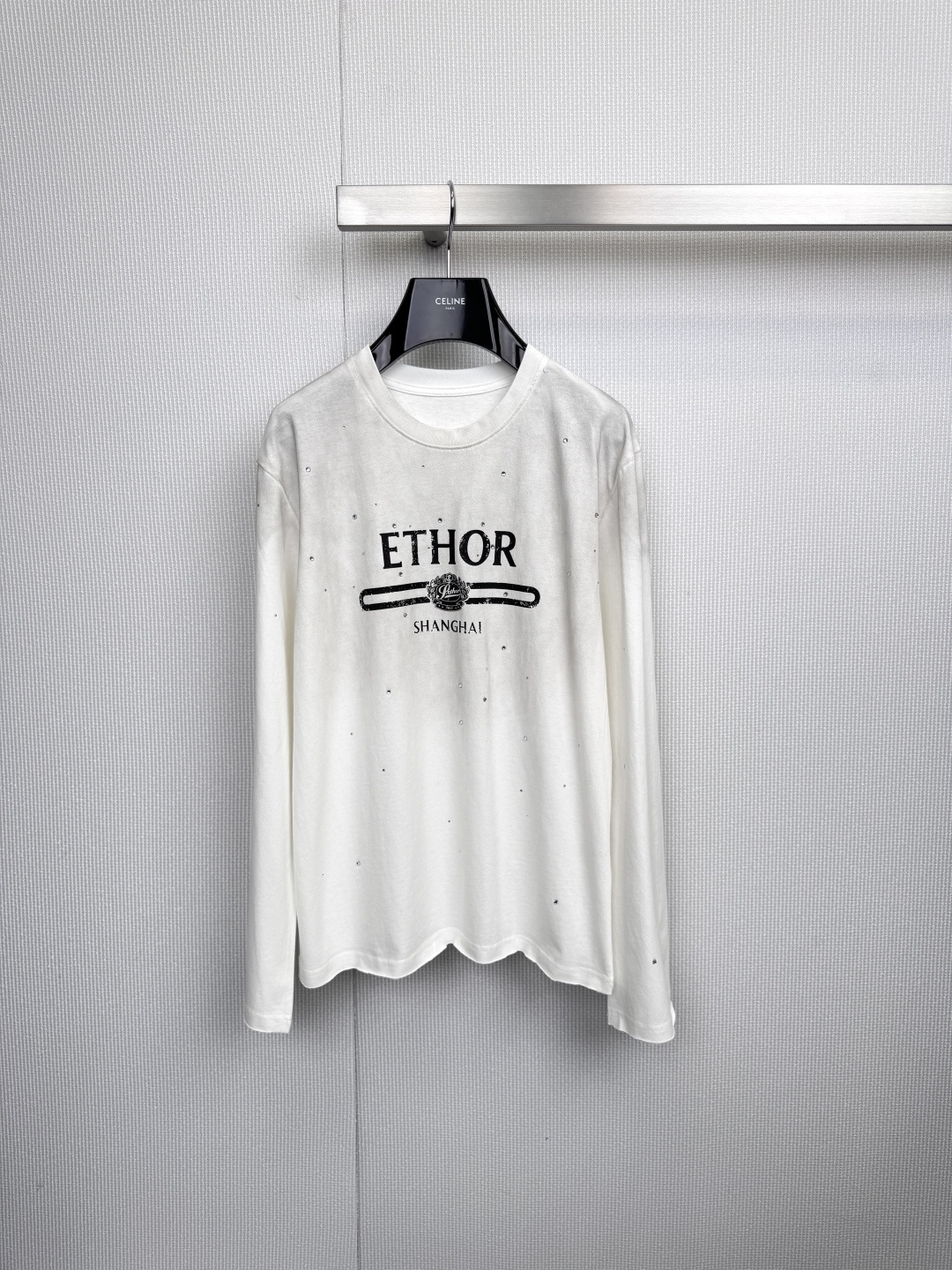 NO:590513,ETHOR long-sleeved T-shirt, urban minimalism, hidden edge, black and white solid color base interprets timeless classics, this ETHOR long-sleeved T-shirt conquers the urban wardrobe with neat tailoring and secret details, 'ETHOR' on the chest  The 'SHANGHAI' logo connects the tension between the brand and the city with a horizontal line, and the exquisite pattern embellished on it is like Morse code, hiding design ingenuity - it is both a visual focus and an identity metaphor. The white model is covered with fine silver sequins, and the light flows like stars and diamonds, which injects low-key luxury into daily wear. The black model uses a matte texture to settle a calm aura, and the dark pattern details inadvertently reveal the pursuit of quality. 1968 is the year the brand was born.  The identity is imprinted on the corners of the clothes, silently telling the fusion of historical heritage and contemporary style. From the hanging aesthetics of the silver hangers to the crisp drape on the upper body, every aspect demonstrates ETHOR's dedication to materials and craftsmanship. Wear it alone with jeans, simple and uninhibited, or layer it with a suit jacket to create depth. This T-shirt is not only a universal cornerstone in the wardrobe, but also a visual poem written for Shanghai's modern life. Size SML,,jeans,jackets  & coats,tees,t-shirt,business suit,alexander wang19860909ETHOR长袖T恤,都市极简主义,暗藏锋芒,黑白纯色基底诠释永恒经典,这款ETHOR长袖T恤以利落剪裁与隐秘细节征服都市衣橱,胸前「ETHOR SHANGHAI」标识以一道横线串联起品牌与城市的张力,点缀其上的精致图案如摩斯密码般暗藏设计巧思——既是视觉焦点,亦是身份隐喻,白色款覆满细密银色亮片,光线流转间似星辰碎钻悄然闪烁,为日常穿搭注入低调奢华,黑色款则以哑光质感沉淀沉稳气场,暗纹细节于不经意间流露品质追求,1968品牌诞生年份烙印于衣角,无声诉说历史底蕴与当代风格的融合,从银色衣架的悬挂美学到上身时的挺括垂坠,每一处皆彰显ETHOR对材质与工艺的执着,单穿搭配牛仔裤简约不羁,内搭西装外套亦可叠出层次深度——这件T恤不仅是衣橱里的万能基石,更是写给上海摩登生活的一首视觉诗.码数SML,,jeans,jackets & coats,tees，t-shirt,business suit,alexander wang,Women's clothing