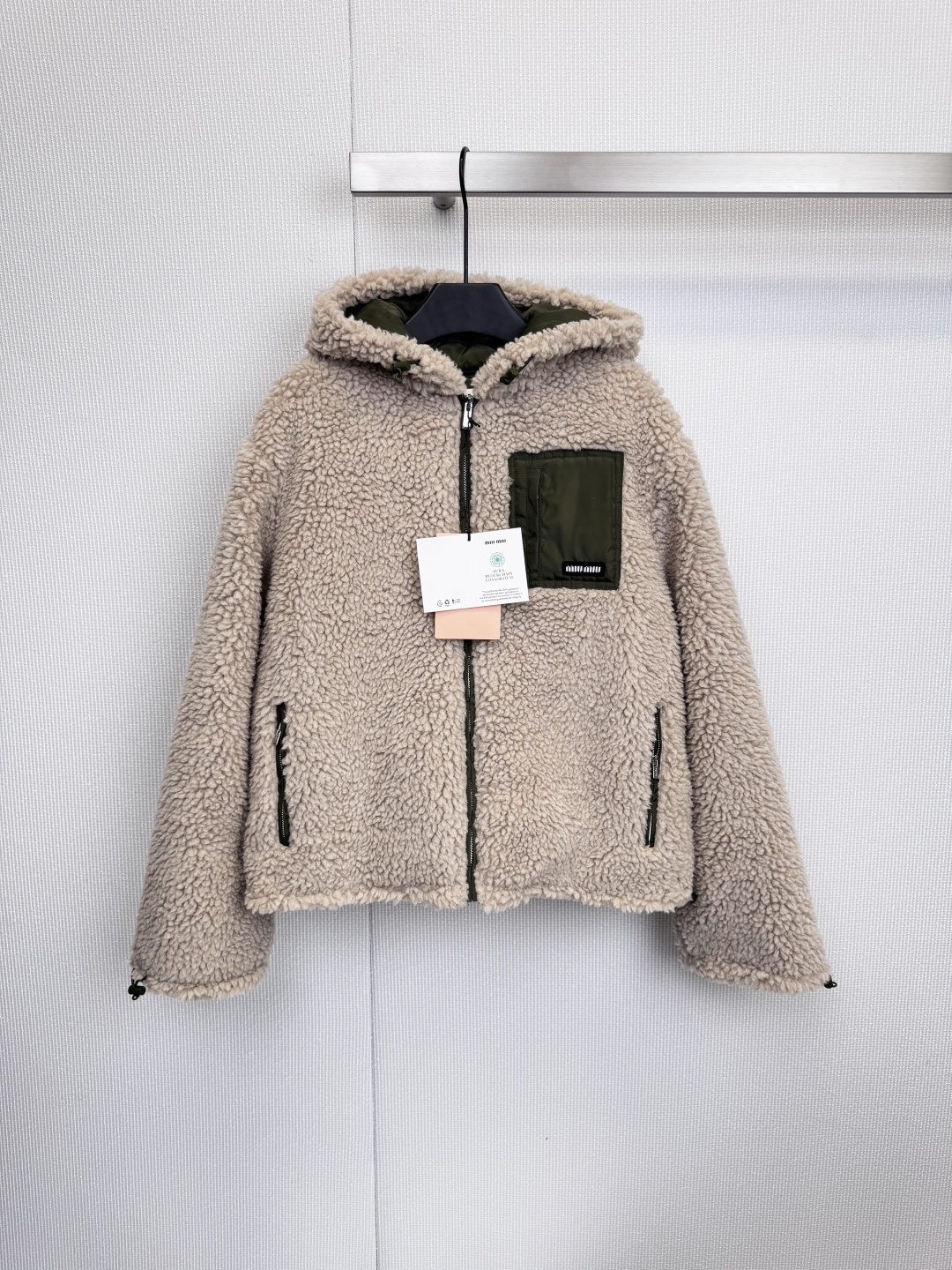 NO:606033,This Miu  The Miu lambswool jacket is the answer to high-end warm winter wear. It skillfully integrates soft touch, lazy silhouette and exquisite details, interpreting effortless fashion, gentle color and texture, and a sense of luxury. The main body is made of warm beige, just like the sunshine in winter, with its own soft light effect, making it appear gentle and very versatile. The use of dark green is the overall design  The soul of the jacket - the hood edges, zippers, pocket piping and the patch pocket on the left chest form a sharp color contrast, instantly breaking the monotony and injecting a touch of retro and vitality. The fluffy and soft lamb wool material not only brings a sense of warmth and security when being wrapped, but also gives the jacket a three-dimensional texture, highlighting the excellent texture of the item. The dark green patch pocket on the left chest is decorated with clear Miu  The Miu brand logo, this low-key logo presentation, is more restrained and advanced. The hooded design adds casualness and protection. The overall silhouette is loose and moderate, which can accommodate the body shape without looking bloated. It perfectly balances fashion and practicality. This jacket perfectly inherits Miu Miu's 'sweet yet cool' style.  The gene, the gentleness of beige and the calmness of green balance each other, the softness of lamb wool and the upright silhouette complement each other. It is a key item that can easily enhance the texture of the overall look. Whether it is paired with a skirt to show the cuteness of a girl, or paired with jeans to show a straightforward side, it can be easily accomplished. Size SML,,miumiu,skirts,jeans,jackets & coats,hats,alexander wang19860909这件Miu Miu羊羔毛外套,堪称冬日温暖的高阶穿搭答案,它巧妙地将柔软触感、慵懒廓形与精致细节融为一体,诠释出毫不费力的时髦感,色彩与质感温柔的高级感,主体选用温暖米色,如同冬日里的阳光,自带柔光效果,显得气质温婉且非常百搭,深绿色的运用是整体设计的灵魂——连帽边缘、拉链、口袋滚边以及左胸的贴袋,形成了鲜明的色彩对比,瞬间打破单调,注入一丝复古与活力,蓬松柔软的羊羔毛材质,不仅带来被包裹的温暖安全感,更赋予了外套立体的肌理感,凸显出单品的优良质感,左胸处的深绿色贴袋上饰有清晰的Miu Miu品牌标识,这种低调的 logo 呈现方式,更显内敛与高级,连帽设计增添了休闲与防护性,整体剪廓形宽松适度,既能包容身形,又不会显得臃肿,完美平衡了时尚度与实穿性,这件外套完美承袭了Miu Miu “甜中带酷” 的基因,米色的温柔与绿色的冷静相互制衡,羊羔毛的软糯与立挺的版型相得益彰,它是一件能轻松提升整体造型质感的关键单品,无论是搭配裙装演绎少女的乖巧,还是搭配牛仔裤展现率性一面,都能轻松胜任.码数SML,,miumiu,skirts,jeans,jackets & coats,hats,alexander wang,Women's clothing