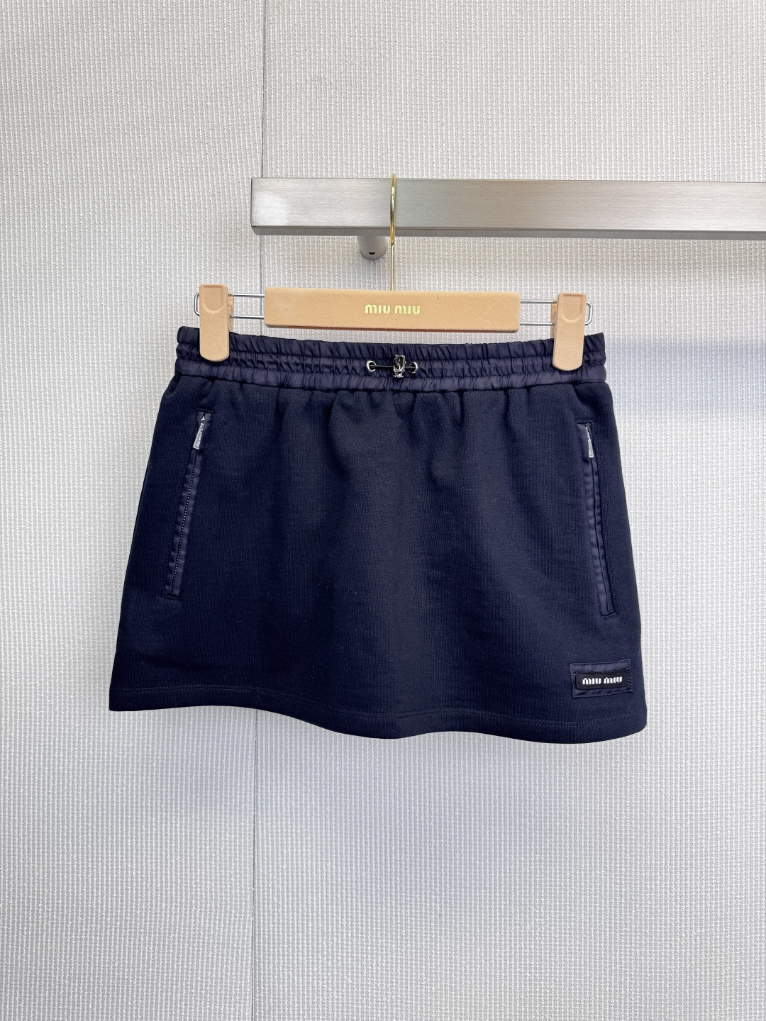 NO:621546,The Miu Miu sports suit is symbolic of fashion and engraved with relaxation in genes. This iconic suit uses deep navy blue as the canvas, perfectly blending street vitality with the exquisite details of high fashion. The short stand-up collar design outlines a neat figure and optimizes body proportions. The brand logo pocket on the left chest is a low-key statement, and the 'miu' digital print throughout the body is like an exclusive password, giving it a unique identity beyond ordinary sportswear.  The digital print that echoes the top wraps around the skirt. The elastic waistband and side zippers cleverly balance wearing comfort and style. The A-line skirt swings lightly with the steps, injecting elegance and agility into the relaxed feeling of movement. There is no need for complicated matching. One set can instantly create a complete look, from jogging in the morning to strolling in the city. With its unique symbolic language and exquisite tailoring, this suit makes you a casual fashion focus in any scene. Size SML  skirt,,miumiu,skirts,alexander wang19860909MiuMiu运动套装,符号化的时髦,刻入基因的松弛,这套标志性套装,以深邃藏蓝为画布,将街头活力与高级时装的精工细节完美融合,短款立领设计,勾勒利落身形,优化身材比例.左胸处的品牌标识口袋是低调的宣言,而贯穿衣身的“miu”数码印花,则如同专属密码,赋予其超越普通运动服的独特辨识度,与上衣呼应的数码印花环绕裙身,松紧腰头与侧边拉链巧妙兼顾穿着舒适度与造型感,A字裙摆随步伐轻盈摆动,在运动松弛感中注入不失优雅的灵动,无需繁复搭配,一套即现完整造型,从晨间慢跑到都市闲逛,这件套装以其独特的符号语言和精致剪裁,让你在任何场景下都成为不经意的时尚焦点.码数SML 半裙,,miumiu,skirts,alexander wang,Women's clothing