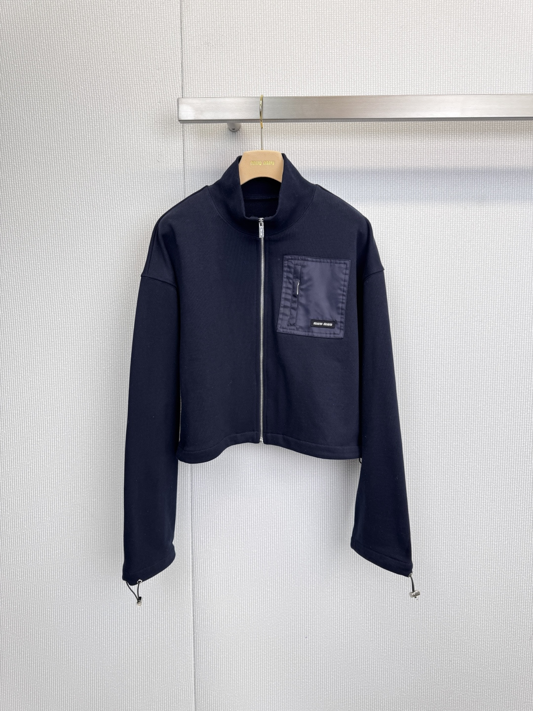 NO:621548,The Miu Miu sports suit is symbolic of fashion and engraved with relaxation in genes. This iconic suit uses deep navy blue as the canvas, perfectly blending street vitality with the exquisite details of high fashion. The short stand-up collar design outlines a neat figure and optimizes body proportions. The brand logo pocket on the left chest is a low-key statement, and the 'miu' digital print throughout the body is like an exclusive password, giving it a unique identity beyond ordinary sportswear.  The digital print that echoes the top wraps around the skirt. The elastic waistband and side zippers cleverly balance wearing comfort and style. The A-line skirt swings lightly with the steps, injecting elegance and agility into the relaxed feeling of movement. There is no need for complicated matching. One set can instantly create a complete look, from jogging in the morning to strolling in the city. With its unique symbolic language and exquisite tailoring, this suit makes you a casual fashion focus in any scene. Size SML  Tops P,,miumiu,skirts,alexander wang19860909MiuMiu运动套装,符号化的时髦,刻入基因的松弛,这套标志性套装,以深邃藏蓝为画布,将街头活力与高级时装的精工细节完美融合,短款立领设计,勾勒利落身形,优化身材比例.左胸处的品牌标识口袋是低调的宣言,而贯穿衣身的“miu”数码印花,则如同专属密码,赋予其超越普通运动服的独特辨识度,与上衣呼应的数码印花环绕裙身,松紧腰头与侧边拉链巧妙兼顾穿着舒适度与造型感,A字裙摆随步伐轻盈摆动,在运动松弛感中注入不失优雅的灵动,无需繁复搭配,一套即现完整造型,从晨间慢跑到都市闲逛,这件套装以其独特的符号语言和精致剪裁,让你在任何场景下都成为不经意的时尚焦点.码数SML 上衣P,,miumiu,skirts,alexander wang,Women's clothing