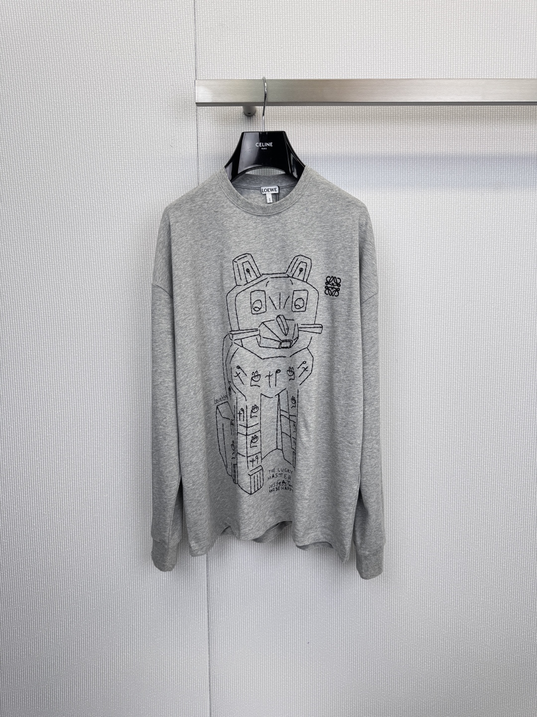 NO:621552,Loewe printed long-sleeved T-shirt, interesting outline, playing with high-end gray. When artistic brushwork meets relaxed daily life, this Loewe gray long-sleeved T-shirt was born. It uses minimalist light gray as the background, carries black line art full of narrative sense, and shows an extraordinary playful attitude in a low-key manner. The cartoon bear pattern on the chest is the overall visual focus. The unique line outline incorporates 'THE LUCK MASTER' and 'REUSE'  The words 'DESIGNER' seem to tell a modern fable about luck, ingenuity and sustainable design. Interesting little handprints and other details inject vitality into the whole. The brand's consistently exquisite cotton fabrics are used to ensure a skin-friendly and soft wearing experience. The loose-fitting tailoring takes into account the comfort of daily wear and effortlessly chic.  Whether it is paired with denim items to create a casual street look, or layered with a suit jacket, this T-shirt can be the finishing touch of the look. This is not just a T-shirt, but also a wearable modern art collection. Size SML, loewe, jackets & coats, tees, t-shirt, business suit, alexander wang19860909Loewe印花长袖T恤,趣意勾勒,玩味高级灰,当艺术笔触遇见松弛感日常,便诞生了这款Loewe灰色长袖T恤,它以极简的浅灰为底色,承载充满叙事感的黑色线条艺术,于低调中展露不凡玩味态度,胸前的卡通熊图案是整体的视觉焦点.独具匠心的线条勾勒,融入“THE LUCK MASTER”与“REUSE DESIGNER”字样,仿佛在讲述一个关于幸运、匠心与可持续设计的现代寓言,趣味的小手印等细节,为整体注入灵动生机,采用品牌一贯考究的棉质面料,确保亲肤柔软的穿着体验.宽松合身的剪裁,兼顾了日常穿着的舒适度与 effortlessly chic 的造型感,无论是搭配牛仔单品打造街头休闲look,还是与西装外套层叠混搭,这件T恤都能成为造型的点睛之笔,——这不仅仅是一件T恤,更是一件可穿着的现代艺术藏品.码数SML,,loewe,jackets & coats,tees，t-shirt,business suit,alexander wang,Women's clothing