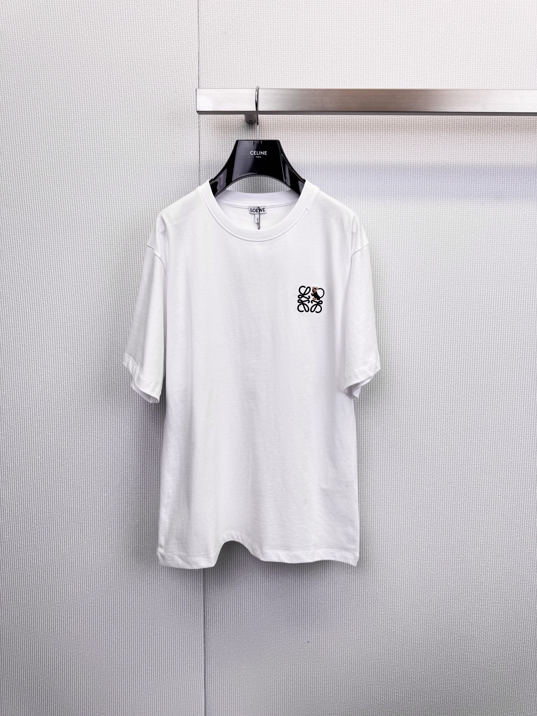 NO:625565,LOEWE embroidered badge T-shirt  , simple style, ingenious branding, iconic embroidery, the finishing touch, the chest is decorated with the LOEWE classic brand logo embroidered badge, and the craftsmanship is exquisitely outlined. The white model uses a bright color combination to rejuvenate, while the black model uses an elegant white and orange color scheme, which is low-key.  Revealing extraordinary taste, every stitch and stitch is a persistent pursuit of texture and details. It uses high-quality cotton fabrics, which are soft to the touch, crisp and stylish. It adheres to the brand's consistent minimalist lines to create a fit that does not pick on your figure. It can be worn alone or layered with a simple style.  About high-end daily styling, the pure white style is refreshing and versatile, the navy style is calm and retro, two classic colors to meet different scenes and dressing needs. Whether it is a casual trip or an elegant gathering, it can become a secret weapon to show your personal style. When LOEWE's exquisite embroidery and CELINE hangers meet unexpectedly, it is like a low-key fashion dialogue, interpreting the indispensable classic items in the modern wardrobe. Size SML, celine, loewe, tees, t-shirt, alexander  wang19860909LOEWE刺绣徽章T恤 ,简约型格,匠心烙印,标志性刺绣,点睛之笔,胸前饰以LOEWE经典品牌标识刺绣徽章,匠心工艺细腻勾勒,白色款采用明快色彩组合,焕发清新活力,黑色款则以雅致白橙配色,低调中流露不凡品味,每一针一线,皆是对质感与细节的执着追求,采用高品质棉质面料,触感柔软且挺括有型,秉承品牌一贯的极简主义线条,打造不挑身材的合身版型,单穿或内搭皆能轻松塑造简约高级的日常造型,纯白款式清爽百搭,藏青款式沉稳复古,两款经典色调,满足不同场景与穿搭需求,无论是休闲出行或雅致聚会,皆能成为彰显个人风格的秘密武器,当LOEWE的精致刺绣与CELINE衣架不期而遇,恰似一场低调的时尚对话,诠释现代衣橱中不可或缺的经典单品.码数SML,,celine,loewe,tees，t-shirt,alexander wang,Women's clothing