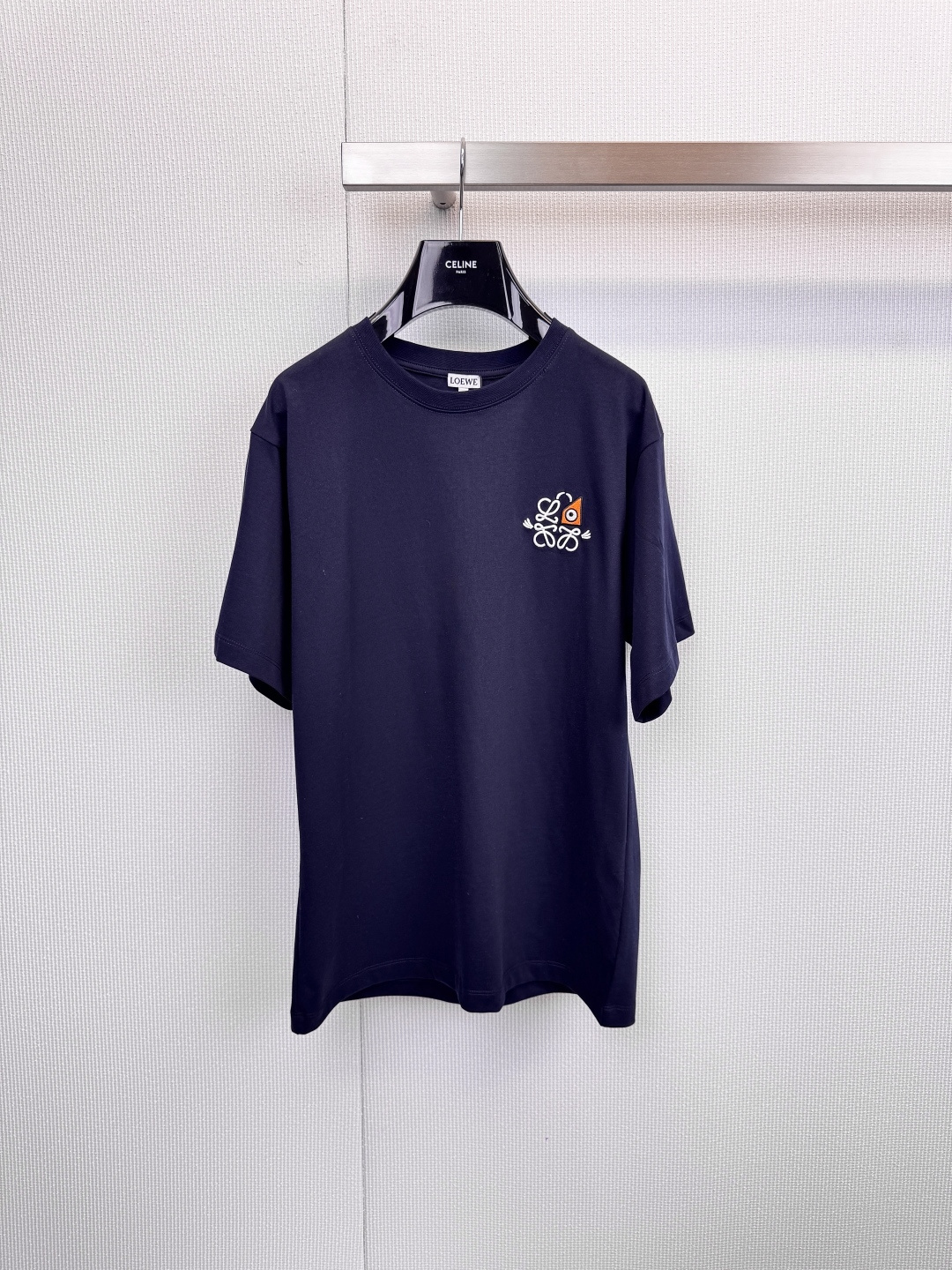 NO:625581,LOEWE embroidered badge T-shirt  , simple style, ingenious branding, iconic embroidery, the finishing touch, the chest is decorated with the LOEWE classic brand logo embroidered badge, and the craftsmanship is exquisitely outlined. The white model uses a bright color combination to rejuvenate, while the black model uses an elegant white and orange color scheme, which is low-key.  Revealing extraordinary taste, every stitch and stitch is a persistent pursuit of texture and details. It uses high-quality cotton fabrics, which are soft to the touch, crisp and stylish. It adheres to the brand's consistent minimalist lines to create a fit that does not pick on your figure. It can be worn alone or layered with a simple style.  About high-end daily styling, the pure white style is refreshing and versatile, the navy style is calm and retro, two classic colors to meet different scenes and dressing needs. Whether it is a casual trip or an elegant gathering, it can become a secret weapon to show your personal style. When LOEWE's exquisite embroidery and CELINE hangers meet unexpectedly, it is like a low-key fashion dialogue, interpreting the indispensable classic items in the modern wardrobe. Size SML, celine, loewe, tees, t-shirt, alexander  wang19860909LOEWE刺绣徽章T恤 ,简约型格,匠心烙印,标志性刺绣,点睛之笔,胸前饰以LOEWE经典品牌标识刺绣徽章,匠心工艺细腻勾勒,白色款采用明快色彩组合,焕发清新活力,黑色款则以雅致白橙配色,低调中流露不凡品味,每一针一线,皆是对质感与细节的执着追求,采用高品质棉质面料,触感柔软且挺括有型,秉承品牌一贯的极简主义线条,打造不挑身材的合身版型,单穿或内搭皆能轻松塑造简约高级的日常造型,纯白款式清爽百搭,藏青款式沉稳复古,两款经典色调,满足不同场景与穿搭需求,无论是休闲出行或雅致聚会,皆能成为彰显个人风格的秘密武器,当LOEWE的精致刺绣与CELINE衣架不期而遇,恰似一场低调的时尚对话,诠释现代衣橱中不可或缺的经典单品.码数SML,,celine,loewe,tees，t-shirt,alexander wang,Women's clothing