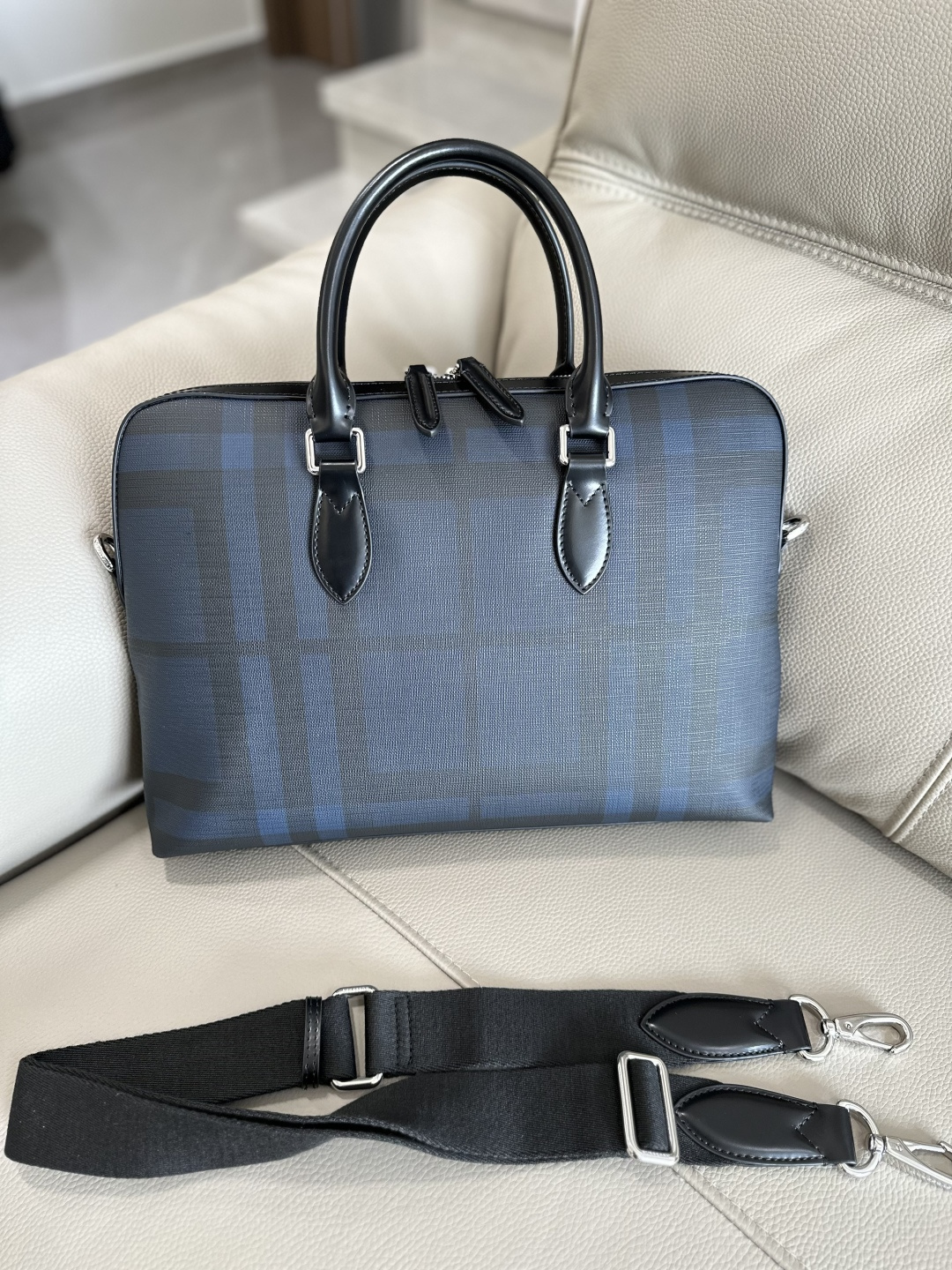 B brand men's briefcase, featuring a selected smoked checkered pattern panel with luxurious leather trim, presenting a structured silhouette. Dimensions 37 x 5.5 x 27cm. Includes zippered inner pocket and slip pockets, detachable and adjustable shoulder strap, zip closure, hand-painted lacquered edges, and glossy metallic hardware. Model number 884155. image 1