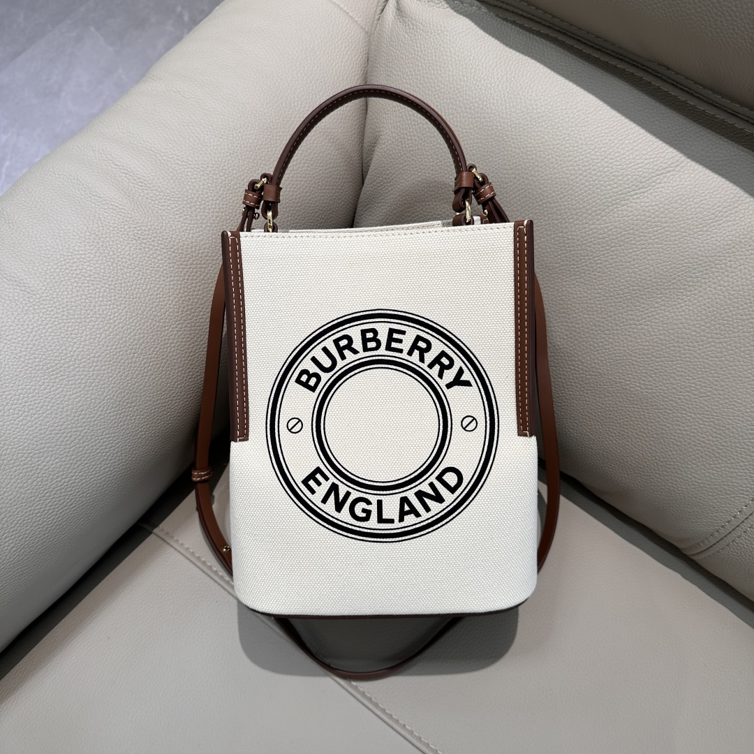 Burberry's equestrian-style cotton canvas bucket bag features contrasting leather edges and embellished with the brand's logo. The compact silhou
