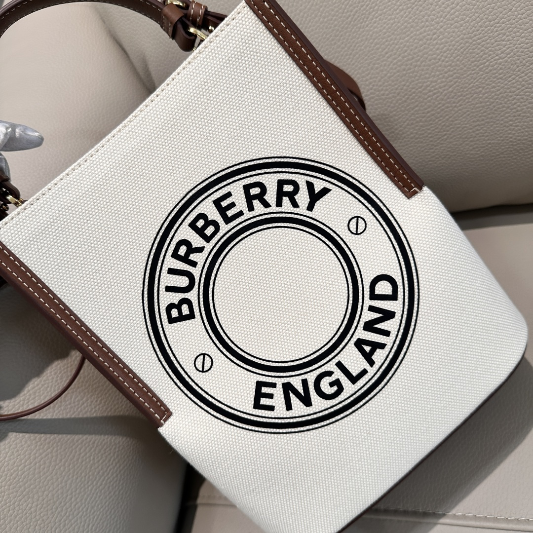 Burberry's equestrian-style cotton canvas bucket bag features contrasting leather edges and embellished with the brand's logo. The compact silhou
