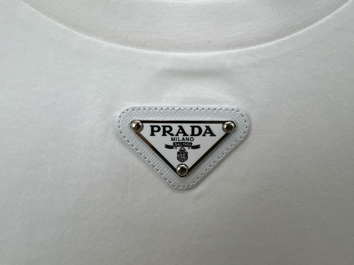 Prada.普拉达 春夏经典标志性的涂珐琅倒三角五金皮章短袖T恤，正面领口处下饰以品牌标志性的涂珐琅三角
