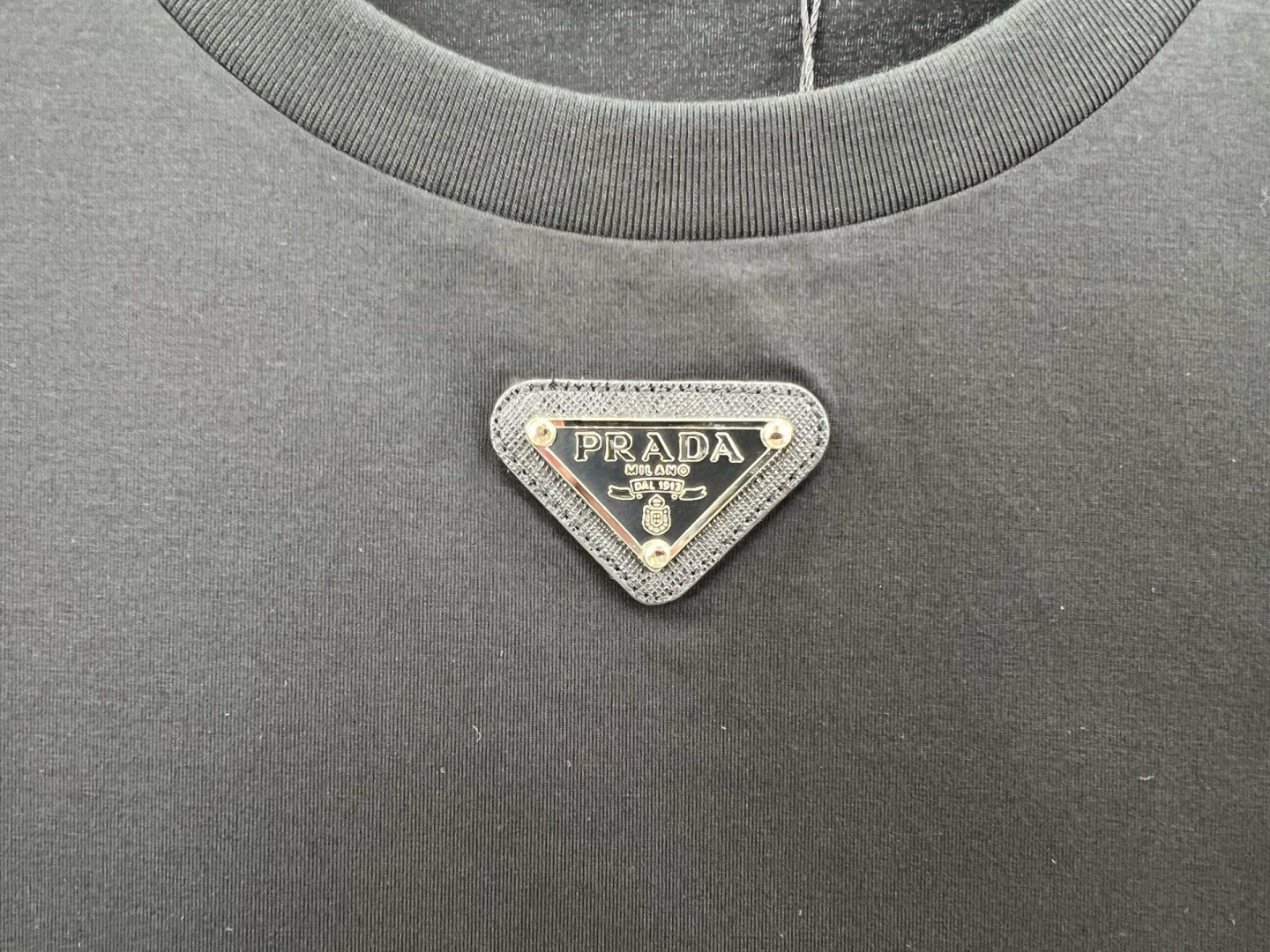 Prada.普拉达 春夏经典标志性的涂珐琅倒三角五金皮章短袖T恤，正面领口处下饰以品牌标志性的涂珐琅三角