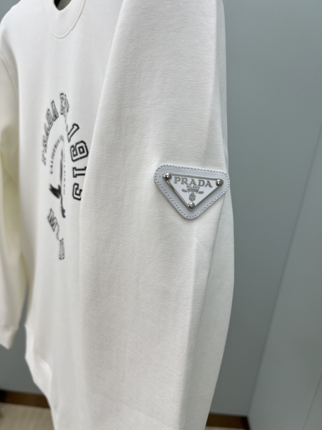 Prada.普拉达 25秋冬新品做旧印花标识针织圆领卫衣，左侧袖臂饰经典涂珐琅三角形金属徽标点缀，采用4