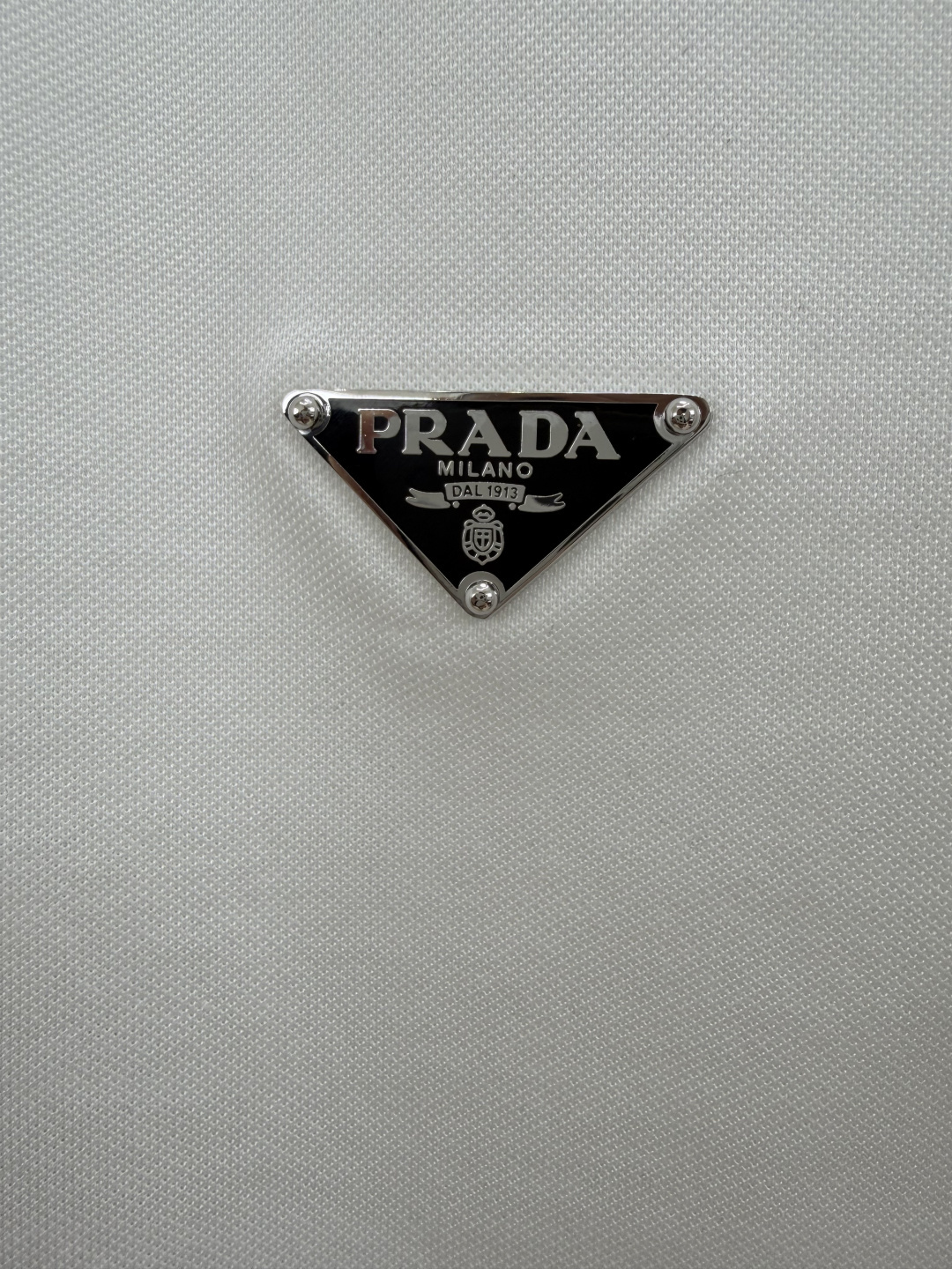 Prada.普拉达 SS26春夏新品经典标识涂珐琅金属三角形徽标Polo衫，以最简约的形式呈现，体现了休