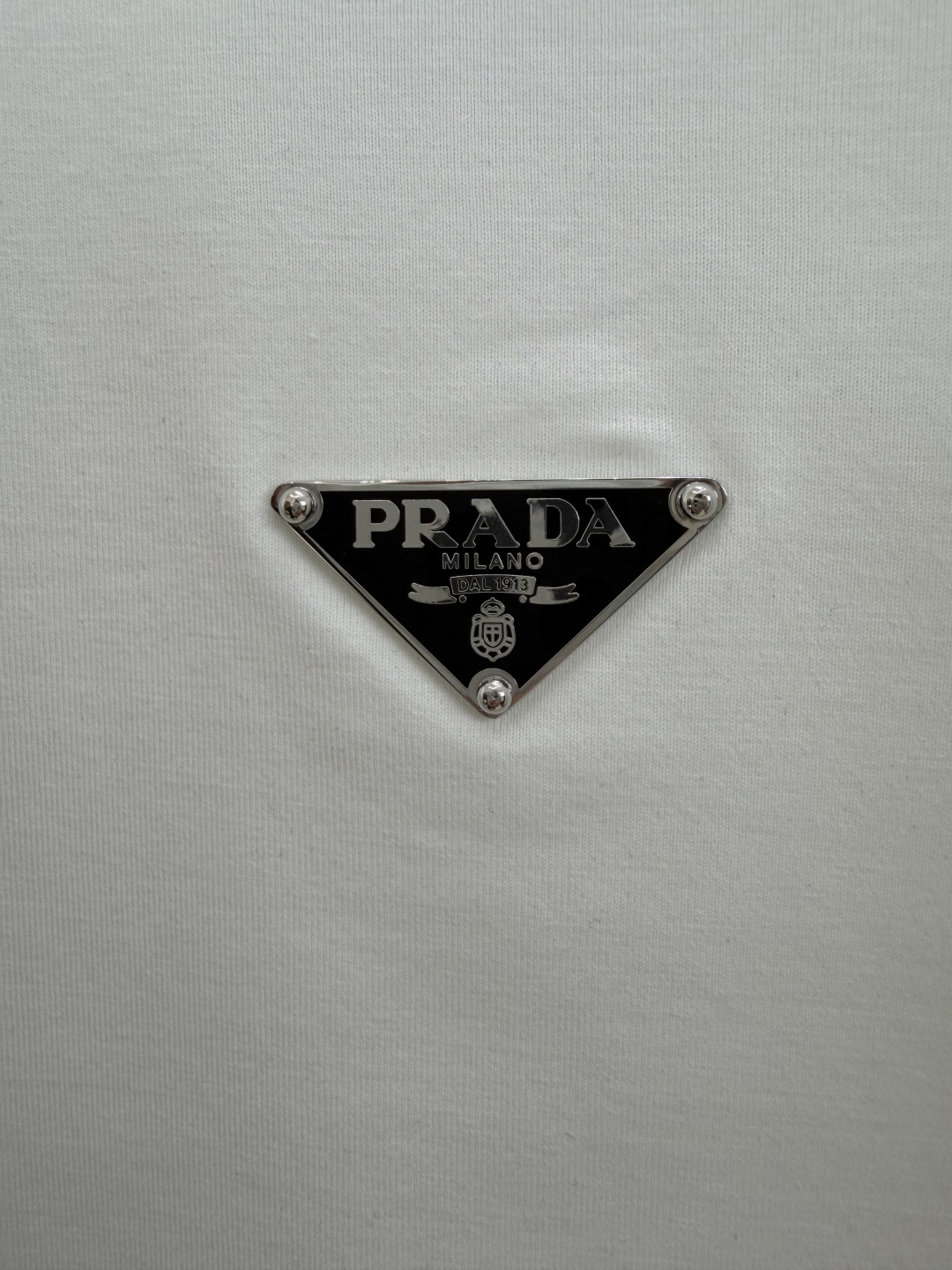 Prada.普拉达 SS26春夏新品经典标识涂珐琅金属三角形徽标短袖T恤，正面胸前饰有品牌经典标志性三角