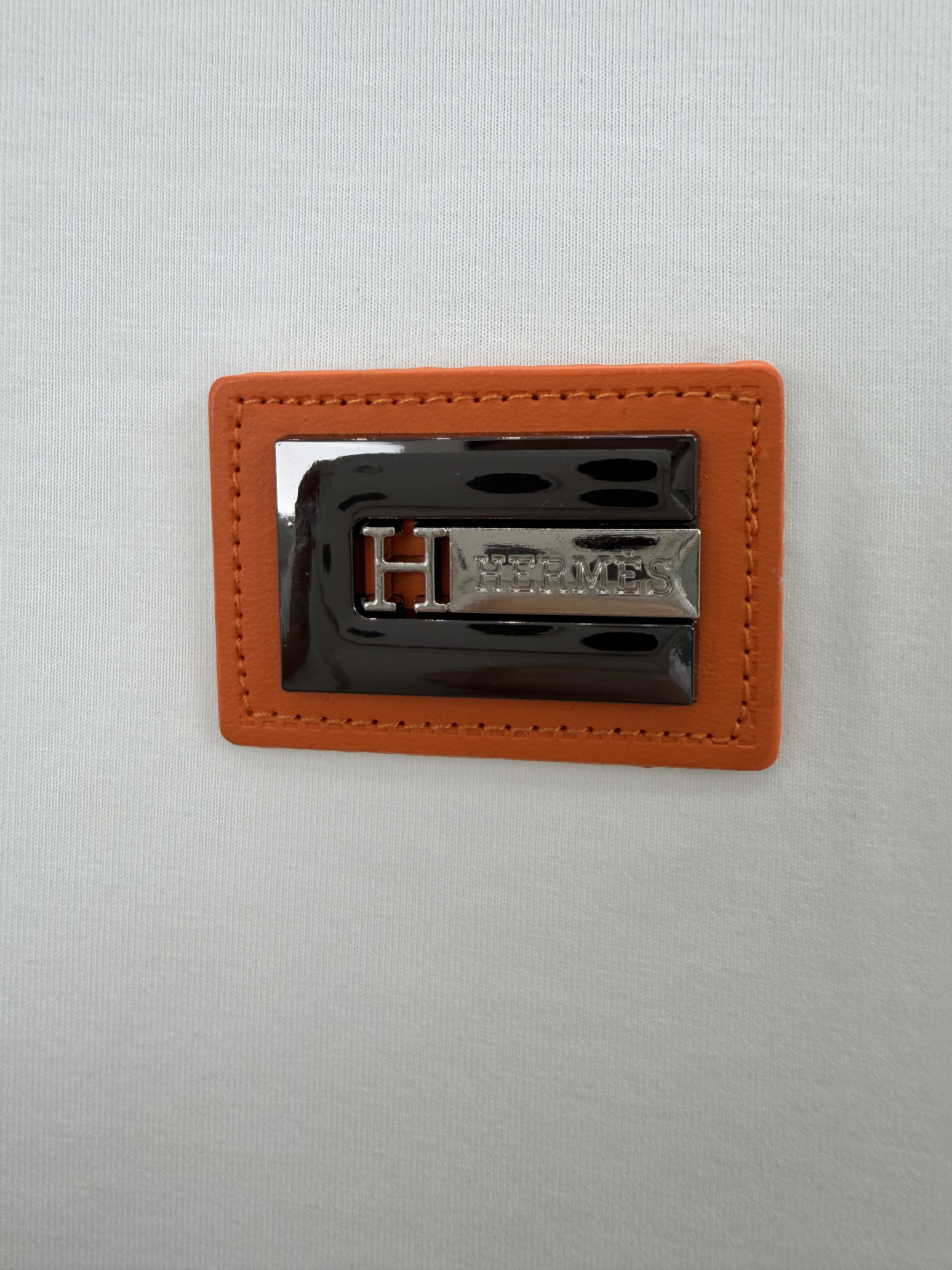 Hermès.爱马仕 SS26春夏新品品牌字母五金皮革徽章短袖T恤，正面胸前饰橙色皮革+品牌字母五金组合