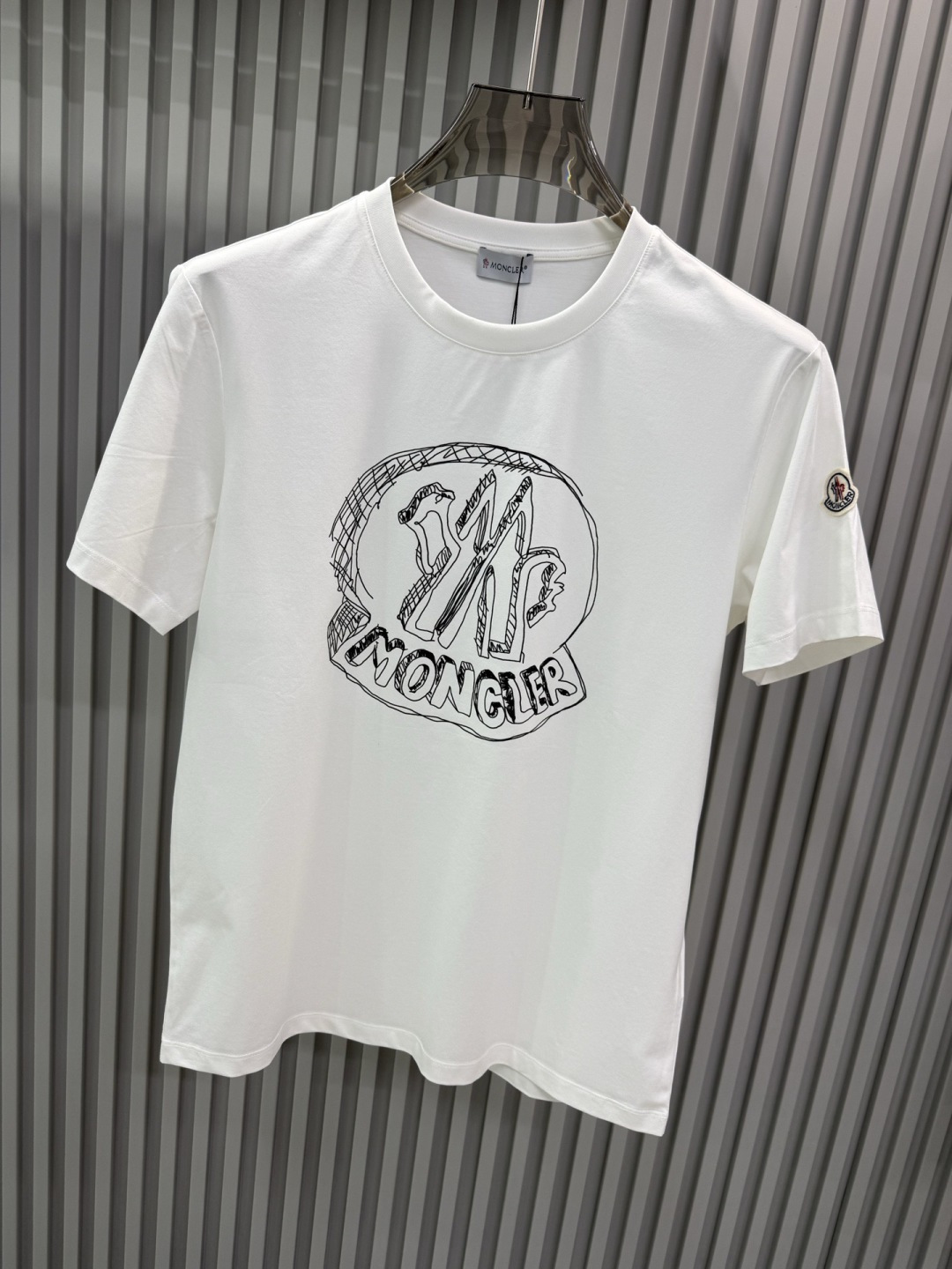 Moncler2026春夏新品抽象印花圆领短袖T恤，主打简约时髦与品牌辨识度的结合。正面采用白色手绘风格