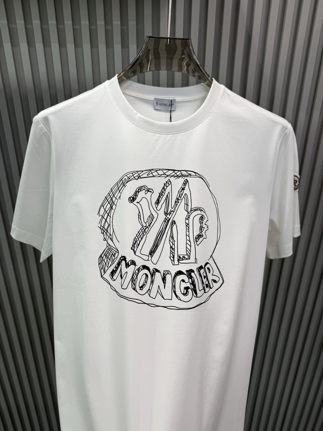 Moncler2026春夏新品抽象印花圆领短袖T恤，主打简约时髦与品牌辨识度的结合。正面采用白色手绘风格