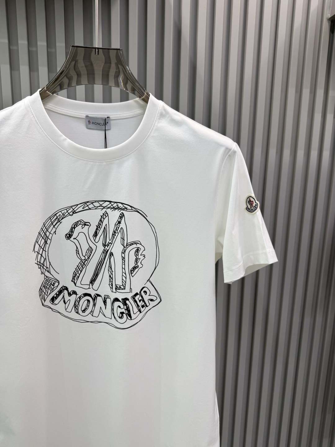 Moncler2026春夏新品抽象印花圆领短袖T恤，主打简约时髦与品牌辨识度的结合。正面采用白色手绘风格