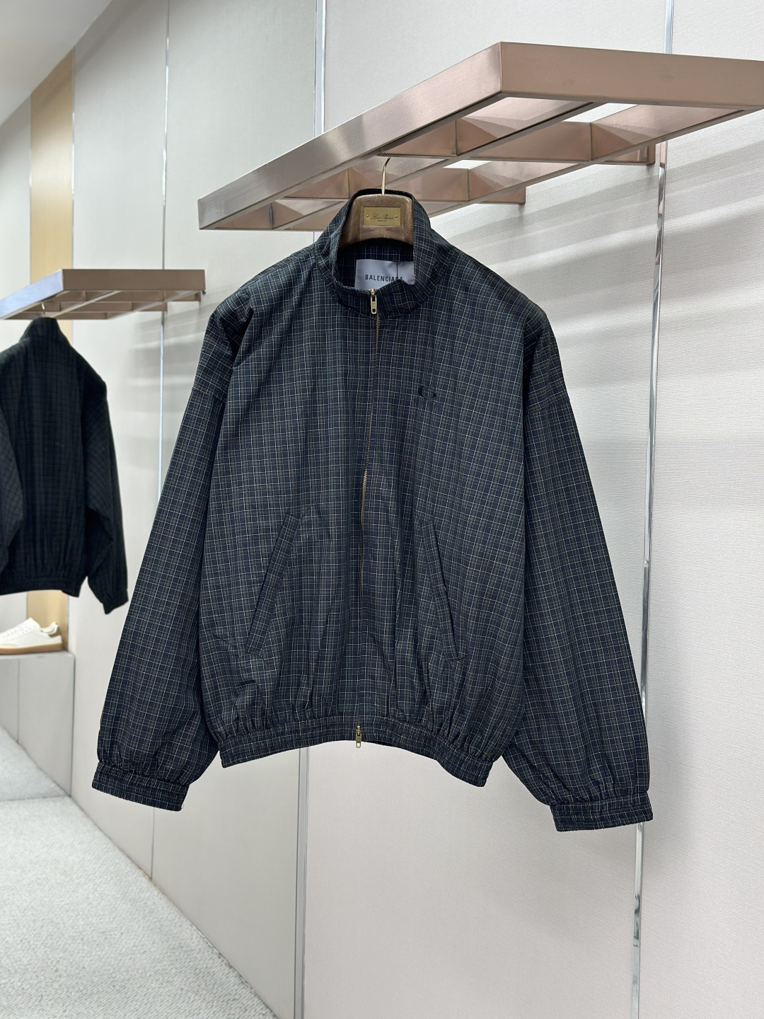 NO:857296,BLCG 26SS two-way zipper closure embroidered plaid jacket  This product is made of custom-made yarn-dyed plaid original fabric. It needs to complete four pre-processing processes of ultra-dense pre-shrinking, weft density correction, tension leveling, and flat-width shaping before being put into production. The shrinkage error of the fabric's longitude and latitude is strictly controlled within 0.2, which completely eliminates the hidden dangers of plaid deformation and alignment deviation after the garment is worn, laying an irreplaceable foundation for the whole piece to align. The pretreatment time of a single fabric is three times that of an ordinary jacket.  The core process difficulty is the full-area interlocking technology, which requires all exposed pieces such as the front and rear panels of the garment, large and small sleeve panels, lapel collars, pocket flap welts, placket stops, and side seam panels to achieve horizontal penetration of horizontal grids, vertical alignment of vertical grids, complete mirror symmetry of left and right panels, and strict alignment tolerances.  It is controlled within 0.1mm, and the industry standard is only 0.5mm. The cutting piece layout adopts zero-loss precise positioning method, and the loss rate of a single fabric is increased by 20. Any deviation of the cutting grain will be judged as a defective product, and the experience and accuracy requirements of the cutting master have reached a strict level.  At the structural level, it is equipped with a two-way double-head customized zipper opening and closing system. The zipper chain and placket pattern need to be 100% aligned in the center seam. When the zipper is installed, the plaid alignment and stop smoothness are simultaneously completed to prevent the plaid from being pulled or skewed due to zipper installation. Front loop  Sportsicon heavy industry embroidery adopts positioning embedded technology. The embroidery stitches must accurately follow the warp and weft direction of the check pattern, and the positioning error of the embroidery frame does not exceed 0.05mm. The floating embroidery process avoids the stitch tension from pulling the fabric texture, and achieves the perfect symbiosis between the embroidery pattern and the check texture.  The entire garment adopts segmented alignment sewing and full-process quality inspection and control. From cutting to finished product, it needs to undergo 7 alignment checks. Every seam, structural line, and decorative piece serves the integrity of the pattern. The complexity of the process, labor cost, and quality control standards are all benchmarked against the high-end garment level. It has both pioneering design and unrepeatable craftsmanship. Sizes 46-52,,jackets & coats,jackets & coats,19860909BLCG 26SS双向拉链开合刺绣格纹夹克外套 本品采用定制色织格纹原布,投产前需完成超密预缩、纬密校正、张力匀整、平幅定型四道前置预处理工序,将面料经纬度缩率误差严控在0.2以内,彻底消除成衣穿着后的格纹形变、对位偏移隐患,为全件对格奠定不可替代的基础条件,单面料预处理工时即为普通外套的3倍. 核心工艺难点为全域贯通对格技术,要求衣身前后片、大小袖片、翻领领面、袋盖贴边、门襟止口、侧缝拼块等所有外露裁片,实现横格水平贯通、竖格垂直对齐、左右片完全镜像对称,对位公差严格控制在0.1mm以内,行业常规标准仅为0.5mm.裁片排料采用零损耗精准定位法,单款面料损耗率提升20,任何一处裁片纹路偏移即判定为次品,对裁剪师傅的经验与精度要求达到严苛级别. 结构层面搭载双向双头定制拉链开合系统,拉链齿链与门襟格纹需实现中缝百分百对齐,拉链安装时同步完成格纹对位与止口平顺处理,杜绝拉链安装导致的格纹拉扯、歪斜.正面loop sportsicon重工刺绣采用定位嵌入式工艺,刺绣针迹需精准贴合格纹经纬走向,绣框定位误差不超过0.05mm,通过浮动刺绣工艺避免针脚张力拉扯面料纹路,实现刺绣图案与格纹肌理的完美共生. 整件成衣采用分段对位缝制、全工序质检管控,从裁片到成品需经过7次对位校验,每一处拼接缝、结构线、装饰件均服务于对格完整性,工艺复杂度、人工成本、品控标准均对标高定成衣级别,兼具先锋设计与不可复制的匠心做工. 尺码46-52,,jackets & coats,jackets & coats,,Men's clothing