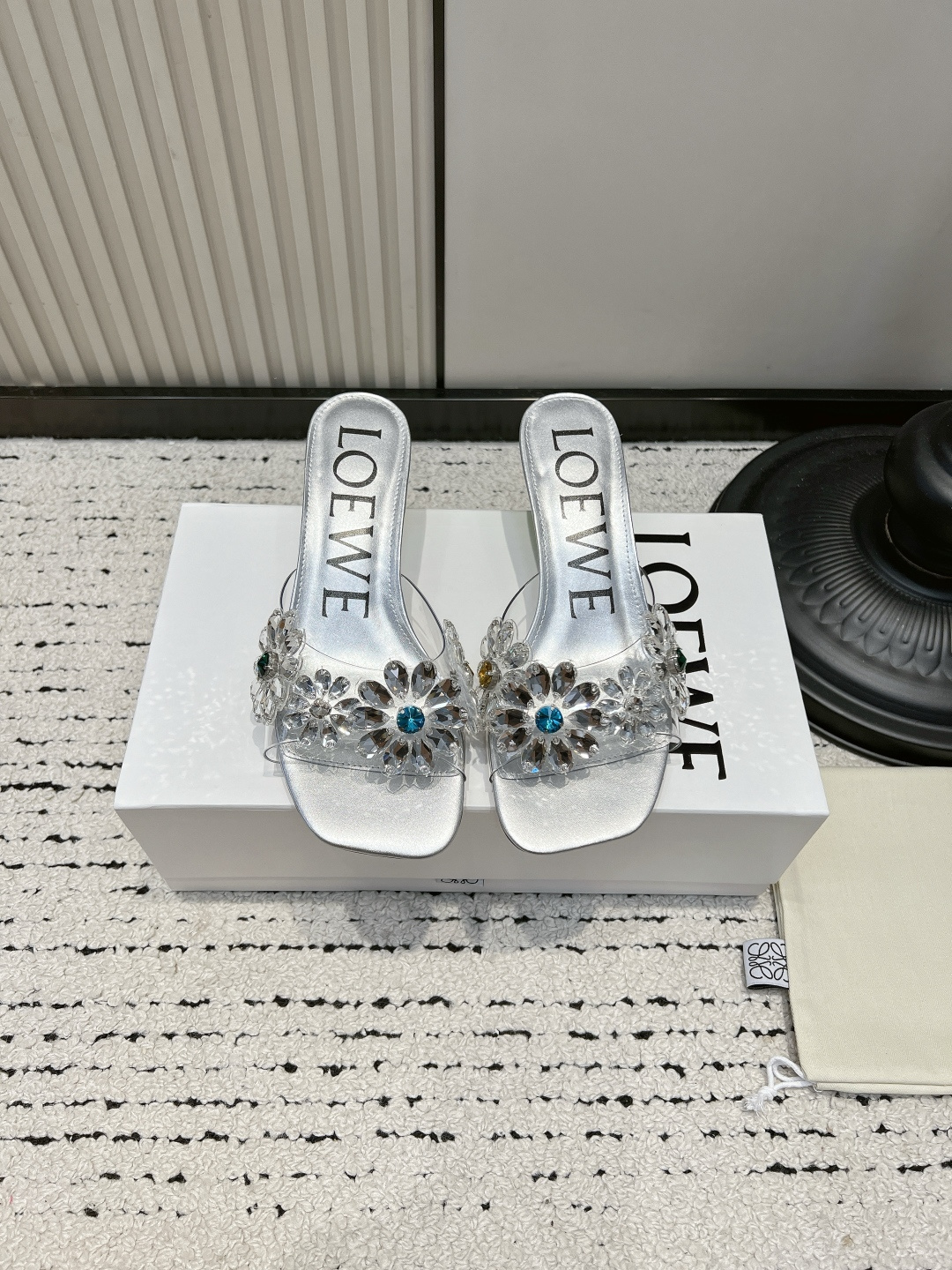 NO:921375,LOEWE 26ss Summer New Rhinestone Transparent Square Toe Sandals This pair of sandals opens up the summer sophistication with its neat square toe silhouette. The transparent upper is studded with three-dimensional rhinestone flowers, and the blue rhinestones in the center are like fine starlight. Every step brings a smart luster, gentle and dazzling. It is suitable for different styles of wear and comes with a high-end soft light filter.  The ingenuity in the details shows the texture. The clear LOEWE logo inside the shoe is matched with exquisite metal accessories. The rhinestones are arranged tightly and firmly and are not easy to fall off. The edges of the square head are polished and smooth without unnecessary rough edges and corners. The low-heeled design combines elegance and practicality and is stable for daily walking. ■Vamp film/diamonds ■Sheepskin lining ■Outsole genuine leather ■Size 35-41 (customized sizes 40 and 41 are not returnable)  ■Heel height 5cm, high heels and slippers, loewe, sandals, high heels, slippers, sheepskin, Leather soles19860909LOEWE 26ss夏季新款水钻透明方头一字凉拖鞋 这双一字拖凉鞋,以利落的方头廓形开启夏日精致感,透明鞋面上缀满立体水钻花朵,中心点缀的蓝调水钻如同细碎星光,每一步都带着灵动的光泽感,温柔又耀眼.适配不同风格的穿搭,自带高级柔光滤镜. 细节处的巧思更见质感,鞋内清晰的LOEWE标识,搭配精致的金属饰件,水钻排列紧密牢固,不易脱落,方头的边缘打磨光滑,没有多余的毛边和棱角,低跟的设计兼顾了优雅与实用性,日常走路也能稳稳当当. ■鞋面胶片/钻 ■内里羊皮 ■大底真皮大底 ■size35-41码（40、41码定制不退换） ■跟高5cm,高跟鞋拖鞋,loewe,sandals,high heels,slippers,sheepskin,Leather soles,Women's Shoes