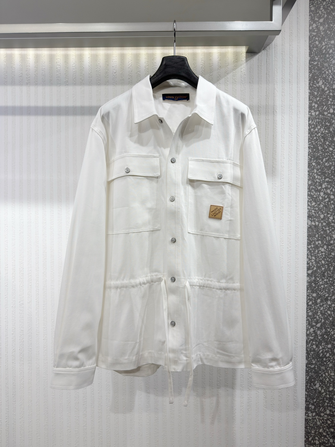 NO:775467,1V 26 leather label printed shirt jacket  This organic cotton shirt jacket perfectly embodies the casual elegance of the Spring/Summer 2026 collection. This versatile, layered piece comes in an understated Greige color with a tonal jacquard herringbone pattern. It features flap pockets on the front and a drawstring at the waist. The left flap pocket is embellished with a natural leather logo patch, while a Vuitton printed logo adds geometric detailing to the back. Sizes S-XL, Louis Vuitton - Clothing, louis vuitton, jackets &  coats,shirts,198609091V 26 皮标印花衬衫外套 这款有机棉质衬衫外套完美彰显2026年春夏系列时装展休闲典雅的格调.此百搭的层次造型单品以低调雅致的Greige色演绎同色调的提花人字纹图案.襟前配上翻盖口袋,腰间设有抽绳.左襟袋点缀天然皮革标志贴章,Vuitton印花标志则为背面添上几何图案细节.尺码S-XL,路易威登-服装,louis vuitton,jackets & coats,shirts,,Women's clothing