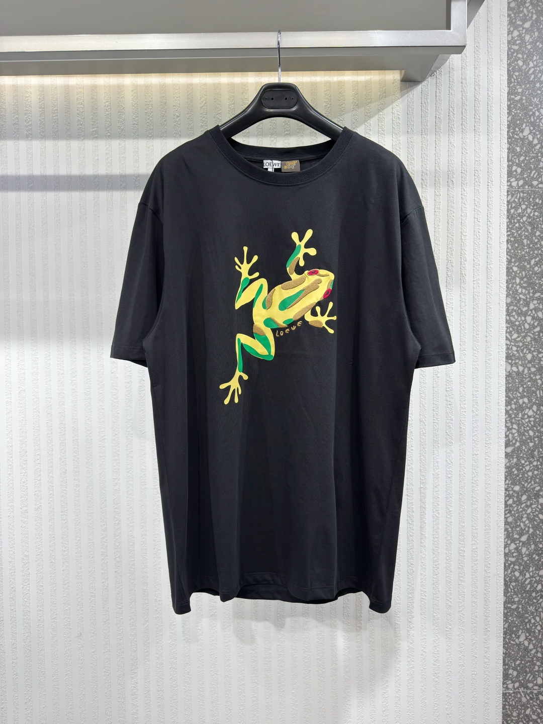 NO:817360,LOEW 26 frog print embroidered round neck short sleeves  Pure cotton knitted fabric, decorated with embroidery and frog prints on the front, Anagram embroidery on the back, standard length, the fabric is tentered and set by a high-temperature setting machine. The warp and weft yarns are restored to straightness and width through tension control, eliminating the previous process.  The generated wrinkles and internal stress create a relaxed and comfortable wearing feeling. The standard length avoids excessive drag and makes the overall proportion more coordinated. Size XS-L, Loewe-clothing, loewe, loewe, T-shirt,19860909LOEW 26 青蛙印绣圆领短袖 纯棉质针织面料、正面饰有刺绣和青蛙印花图案、背面Anagram刺绣、标准长度、面料经高温定型机进行拉幅定形,通过张力控制使经纬纱恢复平直、门幅一致,消除前道工序产生的褶皱与内应力.营造出松弛从容的穿着感.标准长度避免了过长的拖沓感,使整体比例更加协调.尺码XS-L,罗意威-服装,loewe,loewe,T-shirt,,Women's clothing