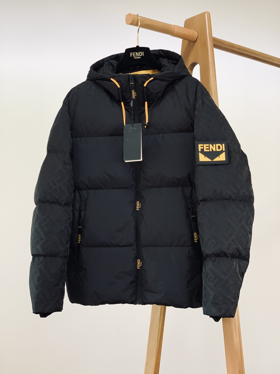 NO:691319,Fendi Fendi 2025FW new autumn and winter product Little Monster Series hooded down jacket. The lining is filled with 90% white duck down. The down has high fluffiness and excellent resilience. The temperature locking performance is far superior to ordinary down. The lightweight filling design eliminates the bloated feeling. It can lock in heat in low temperature weather and maintain a neat wearing posture. It has both warmth and style.  The sleeves and brim are spliced with classic FF presbyopic dark pattern fabric, which hides brand recognition in a low-key manner. The matte texture and the glossy body form a visual contrast, adding a sense of layering; the yellow and black contrasting rubber badges on the arms incorporate FD's iconic little monster design language, and the three-dimensional relief texture is prominent, becoming a cool highlight of the overall look; The placket and pockets are all made of metal zippers engraved with the brand's letter logo, which are smooth and thick in texture, and the hardware details highlight the level of light luxury craftsmanship;  The inside of the body is lined with bright yellow, which creates a strong contrast with the black outer body. The zipper instantly reveals the ingenuity, and the details are full of style. The loose hooded silhouette is not flattering, and the black main color is classic and versatile. It can be worn with jeans to create a casual street style, or with trousers to unlock a light and luxurious commuting style. It is a high-end trendy item that combines warmth and appearance in autumn and winter. …………………………………………………… Size48-56,,fendi,fendi,jeans,down  jacket,hats,19860909Fendi 芬迪 2025FW秋冬新品 小怪兽系列连帽羽绒服.内胆填充90白鸭绒,绒朵蓬松度高、回弹性优异,锁温性能远超普通羽绒,轻量化填充设计告别臃肿感,低温天气里既能锁住热量,又能保持利落的穿着体态,保暖与造型感两不误. 袖子与帽檐拼接经典FF老花暗纹面料,低调中暗藏品牌辨识度,哑光质感与亮面衣身形成视觉对比,层次感拉满； 手臂处的黄黑撞色橡胶徽章,融入FD标志性小怪兽设计语言,立体浮雕质感突出,成为整体造型的潮酷亮点； 门襟与口袋均采用刻有品牌字母标识的金属拉链,拉合顺滑且质感厚重,五金细节彰显轻奢工艺水准； 衣身内侧采用明黄色衬里,与黑色外身形成强烈撞色,拉开拉链瞬间展露巧思,细节处尽显格调. 宽松的连帽廓形版型不挑身形,黑色主调经典百搭,搭配牛仔裤可打造街头休闲风,配西裤则解锁轻奢通勤造型,是秋冬兼具保暖与颜值的高端潮搭单品. …………………………………………………… Size48-56,,fendi,fendi,jeans,down jacket,hats,,Men's clothing