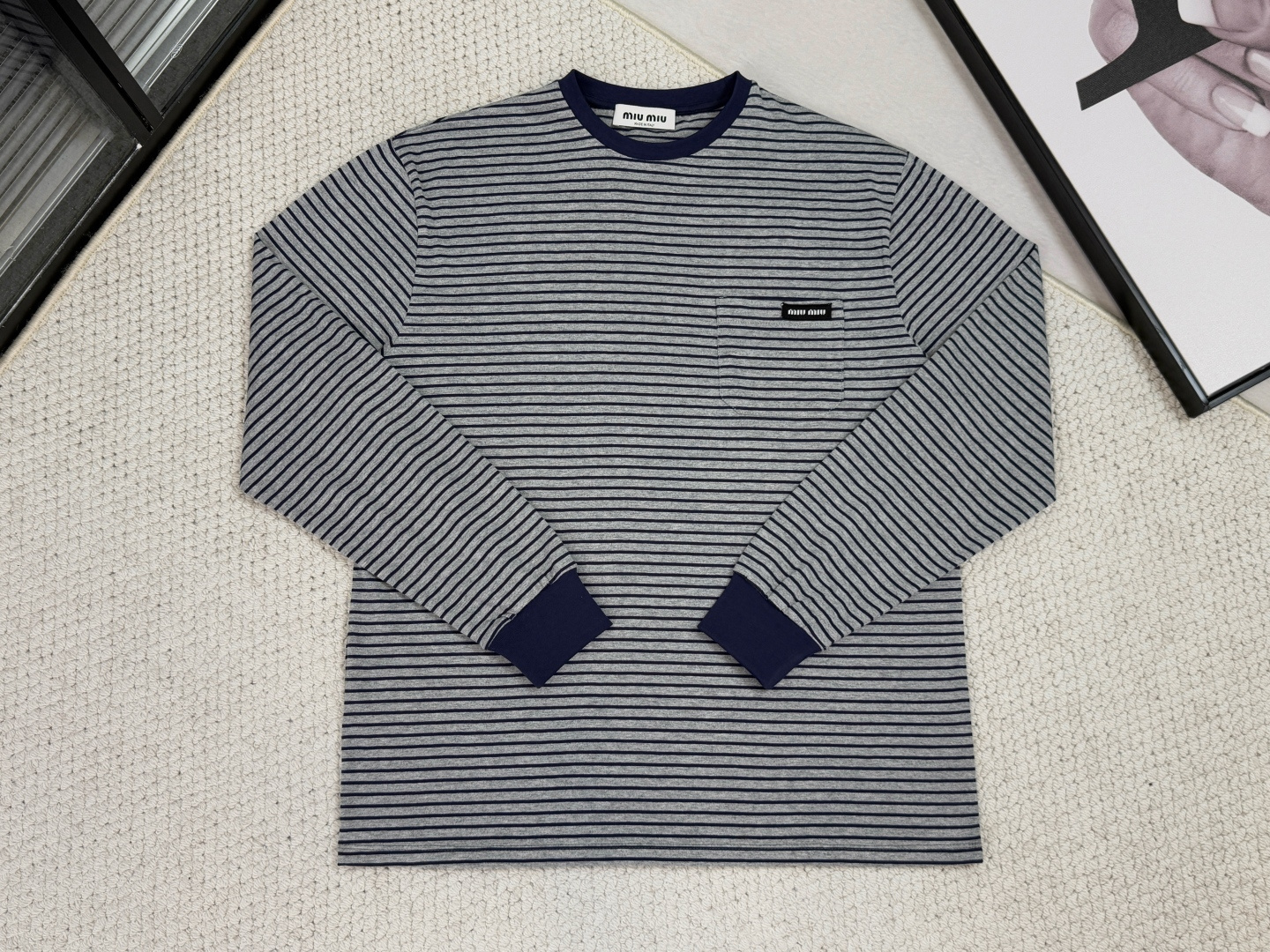 NO:540146,-MiuMiu-Product Introduction MM / Striped jersey long sleeve fabric 24S jacquard special textile tight cotton / 185G ribbed 32S double yarn pull rack / 380G fabric layer, the main body is made of 24 tight spun cotton, and a jacquard base fabric of 185g/square meter through special textile technology. The tight spun technology makes the yarn hair less and the strength is high, and the fabric structure is particularly dense and flat, with a delicate and skin-friendly touch and excellent anti-pilling and wear resistance, laying the foundation for the durability and texture of a single product beyond ordinary cotton fabrics.  In terms of structural technology, 32 double yarn pull-up ribs are used in key easily deformed parts such as necklines and cuffs. The high-strength double yarn gives the ribs an extremely delicate texture. The high-strength double yarns combine with the addition of spandex to make it have a heavy skin and strong elasticity, ensuring the long-lasting and crisp shape of the garment and effectively preventing loose deformation. The stripes woven by color yarns form subtle layers with the potential base cloth jacquard texture. The stripes are formed integrally by different color yarns when weaving, with extremely high color fastness and clear and neat edges. The overall abandonment of redundant decoration, making the superiority of the material itself a visual focus, and creating a fine product that is outstanding in comfort, durability and simplicity.,,miumiu,alexander wang19860909-MiuMiu-产品简介 MM / 条纹平纹针织长袖 面料24S提花特种纺织紧密棉 / 185G 罗纹32S双纱拉架 / 380G 面料层面,主体采用24支紧密纺棉,通过特种纺织工艺制成185克/平方米的提花底布.紧密纺技术使纱线毛羽少、强度高,织出的面料结构尤为密实平整,兼具细腻亲肤的触感与出色的抗起球耐磨性能,奠定了单品超越普通棉织物的耐用性与质感基础. 结构工艺上在领口、袖口等关键易变形部位,采用32支双纱拉架罗纹.高支双纱赋予罗纹极致细腻的纹理,高克重配合氨纶的加入,使其具备重磅的骨感与强大的回弹性,确保衣身廓形持久挺括,有效防止松懈变形. 通过色纱编织的条纹与潜在的底布提花纹理形成微妙层次.条纹由不同色纱在织造时一体成型,色牢度极高且边缘清晰利落.整体摒弃冗余装饰,让材质本身的优越性成为视觉焦点,成就了一款在舒适度、耐用性与简约风格上均表现出众的精品.,,miumiu,alexander wang,Men's clothing