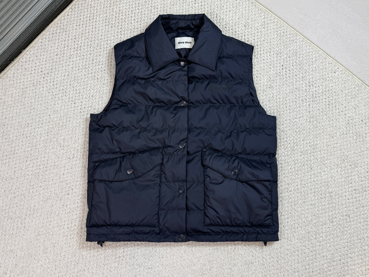 NO:610190,Miu Miu-MM / Quilted Down Vest This down vest reinterprets outdoor style through functional technical fabrics and styling research and can be worn alone or as an inner layer in bold combinations.  It uses ultra-light recycled polyester fiber as the base material and is treated with Teflon ecological coating to achieve level 5 water-repellent performance. It is filled with national standard certified white goose down and forms an independent temperature-controlled cabin through a three-dimensional vertical lining structure, which can still maintain core body temperature stability in low temperature environments. The surface of the fabric is treated with microporous moisture permeability, and the moisture transmittance can reach 5L/㎡·24h. The inner lining is made of anti-static warp and weft knitted fabric to eliminate static electricity problems caused by down friction.  The logo uses a vintage lamination transfer process, and by regulating the hot pressing temperature in the 115-125°C range, the polyurethane film shows a micro-cracked texture that has been used for many years. The edges of the pattern are precisely laser etched to ensure that the intact shape remains intact in extreme environments.  It innovatively adopts the grafting process of shirt collar shape and outdoor function. The collar has a built-in flexible support piece to ensure that the collar remains elegant and straight in any stacking state. The front placket is equipped with 5 sets of opening and closing buttons, which can be opened and closed multiple times to maintain a bite strength of 94, allowing for a second-level putting on and taking off experience.  The flap pocket uses three-dimensional molding technology, and the opening and closing buttons are integrated into the three-dimensional bag cover through eight processes. The hem has a built-in elastic drawstring structure, using a core-spun rope and a self-locking adjuster, and the windproof sealing adjustment can be completed with one hand.,,miumiu,shirts,down jacket,alexander wang19860909Miu Miu-MM / 绗条羽绒背心 这款羽绒背心通过功能性技术面料和造型研究重新诠释户外风格,可单独穿着或作为内层搭配大胆组合. 选用超轻再生聚酯纤维作为基材,经特氟龙生态涂层处理实现5级防泼水性能.内充国标认证白鹅绒,通过立体立衬结构形成独立温控舱室,在低温环境下仍能保持核心体温稳定.面料表面进行微孔透湿处理,湿气透过率可达5L/㎡·24h.内衬使用抗静电经纬编面料,消除羽绒摩擦产生的静电困扰. 徽标采用复古压胶转印工艺,通过调控热压温度在115-125℃区间,使聚氨酯薄膜呈现经年使用的微裂纹理.图案边缘进行精准激光蚀刻,确保在极端环境下仍保持完整形态. 创新采用衬衫领型与户外功能的嫁接工艺,领座内置柔性支撑片,确保领口在任何叠穿状态下保持优雅立挺.前襟配置5组开合纽扣,多次开合保持94的咬合力度,实现秒级穿脱体验. 翻盖口袋运用三维成型技术,通过八道工序开合纽扣整合在立体袋盖上.下摆内置弹力抽绳结构,采用包芯绳与自锁调节器,单手即可完成防风密封调节.,,miumiu,shirts,down jacket,alexander wang,Men's clothing