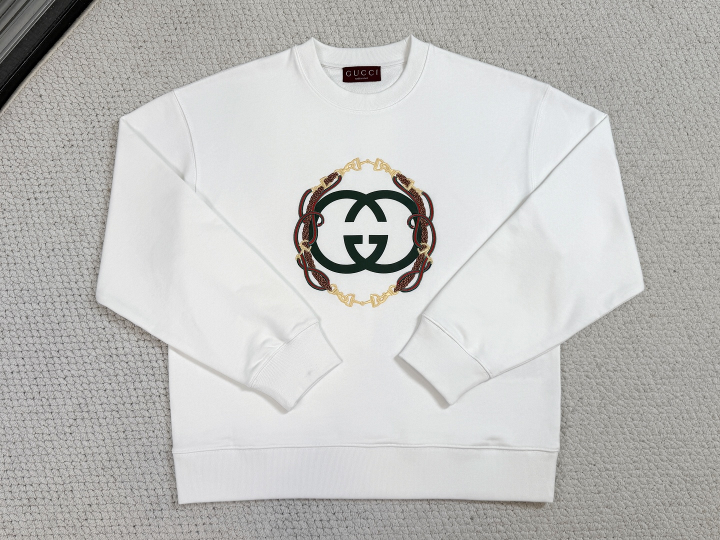 NO:712304,Gucci/Product Introduction GC / Embroidered knitted cotton sweatshirt Fabric 26 count double yarn top layer fish scale terry bottom / 380G Rib 21 count 1x1 rib / Weight 470G  It adopts a 26-count double-yarn fish-scale bottom structure, and its heavy weight creates a sculptural and crisp silhouette. The fish-scale bottom layer is precision brushed to form a 1.5mm thick suede surface, achieving the ultimate balance of external bone texture and internal cloud velvet touch. The cuffs and hem are matched with 21 super-heavy ribs, and its anti-deformation coefficient is significantly higher than that of conventional fabrics, ensuring a stable shape after multiple wears and washes.  The innovative use of elastic glue printing + needle embroidery dual process superimposition first uses environmentally friendly elastic paste to print the interlocking double G base, showing a semi-matte flexible texture; then uses 14 stitches per centimeter of needle embroidery to outline the reins webbing, and the embroidery threads are accumulated to form a 1.2mm three-dimensional relief effect. The two processes visually form a layered dialogue between planes and convexes, and are both soft and solid to the touch.  The round-neck drop-shoulder cut uses three-dimensional shoulders and moderate bust relaxation to maintain neat lines while leaving room for movement. The neckline uses a double-layer fabric binding process, and elastic yarn is embedded inside to ensure the collar shape is durable. All seams are reinforced with four-line overlocking, and the internal seams are processed by ultrasonic trimming to avoid friction and discomfort caused by suede fabrics.,,gucci,hoodie,sweatshirts,19860909Gucci古奇/产品简介 GC / 刺绣针织棉卫衣 面料26支双纱面层支纱鱼鳞毛圈底 / 380G 罗纹21支1x1罗纹 / 克重470G 采用26支双纱面层支纱鱼鳞底结构,重磅克重成就其雕塑般挺括轮廓.鱼鳞状底层经精密刷绒形成1.5mm厚绒面,实现外部骨感与内部云绒触感的极致平衡.袖口及下摆搭配21支超重磅罗纹,其抗变形系数较常规面料明显提升,确保多次穿洗后形态稳定. 创新采用弹力胶浆印花+挨针刺绣双工艺叠加先以环保弹力浆料印制互扣双G基底,呈现半哑光柔韧质感；再以每厘米14针的挨针绣勾勒缰绳织带,绣线堆积形成1.2mm立体浮雕效果.两种工艺在视觉上形成平面与凸起的层次对话,触感上兼具柔软与扎实. 圆领落肩剪裁通过立体肩部与适度胸围放松量,在保持利落线条的同时预留活动空间.领口采用双层面料包边工艺,内部嵌入弹力纱线确保领型持久.所有接缝采用四线锁边加固,内部缝份经超声波切边处理,避免绒面面料产生摩擦不适.,,gucci,hoodie,sweatshirts,,Men's clothing