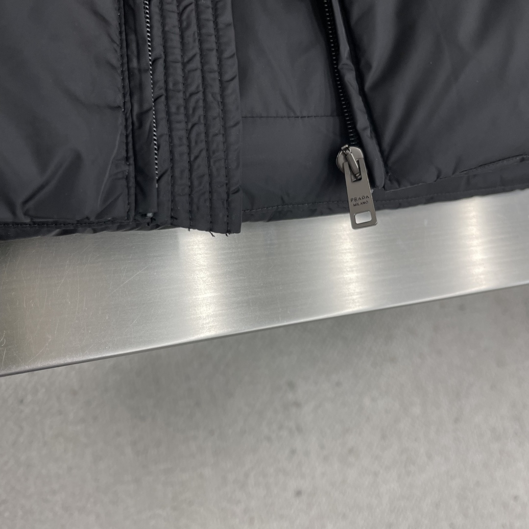 -PRAD 新款三角微标羽绒服。这款羽绒服采用新国标90白鸭绒填充而成，拉链式开合，前胸搭配有三角微标，