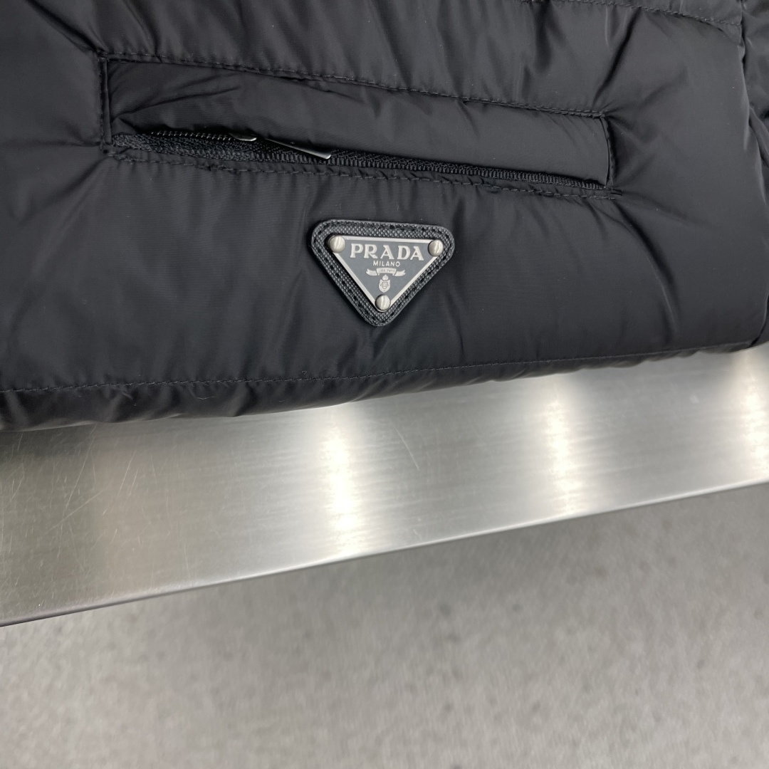 -PRAD 新款三角微标羽绒服。这款羽绒服采用新国标90白鸭绒填充而成，拉链式开合，前胸搭配有三角微标，