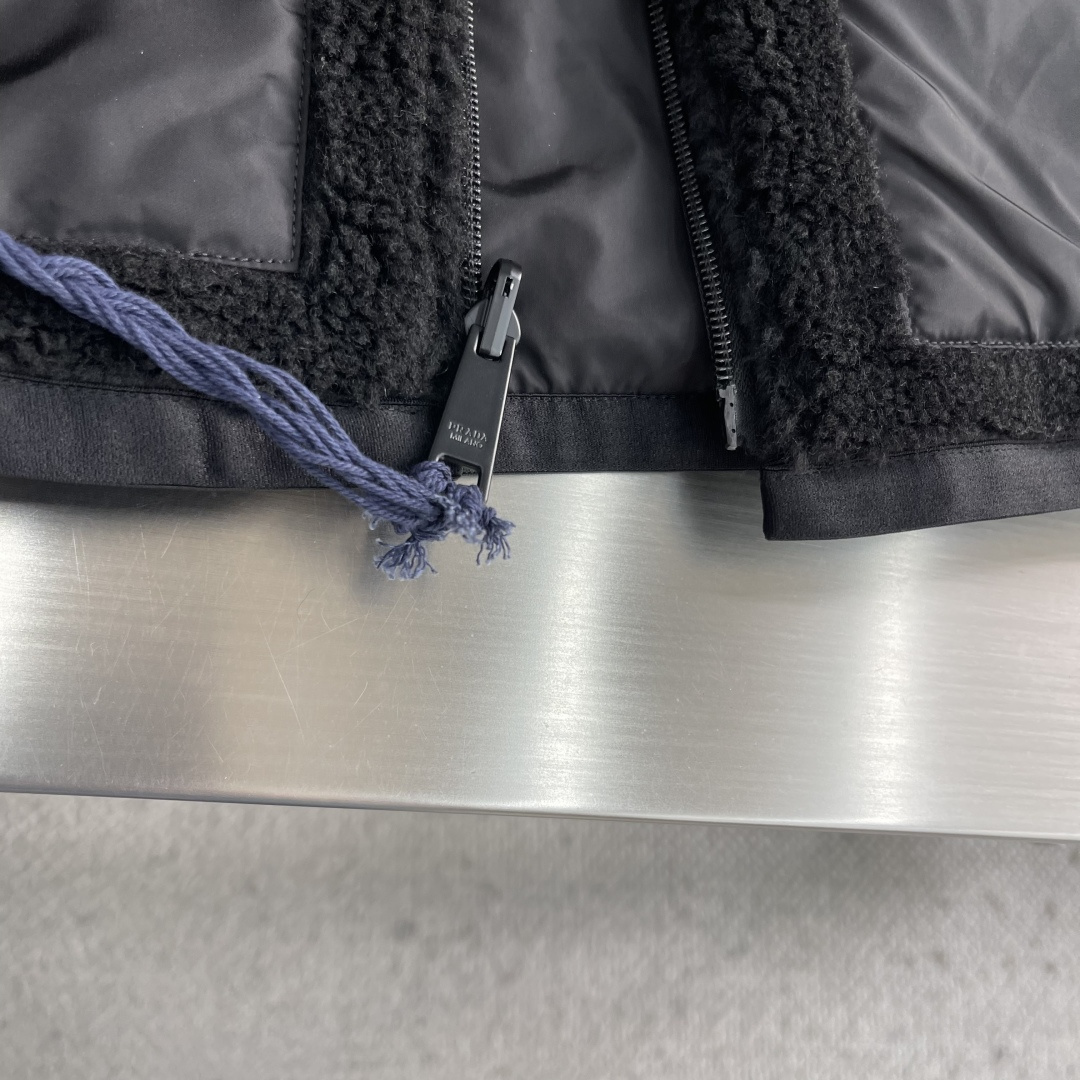 -PRAD 新款双面穿连帽夹克。这款夹克采用摇粒绒与防风面料拼接设计，兼具保暖性与机能感。胸前红色品牌标