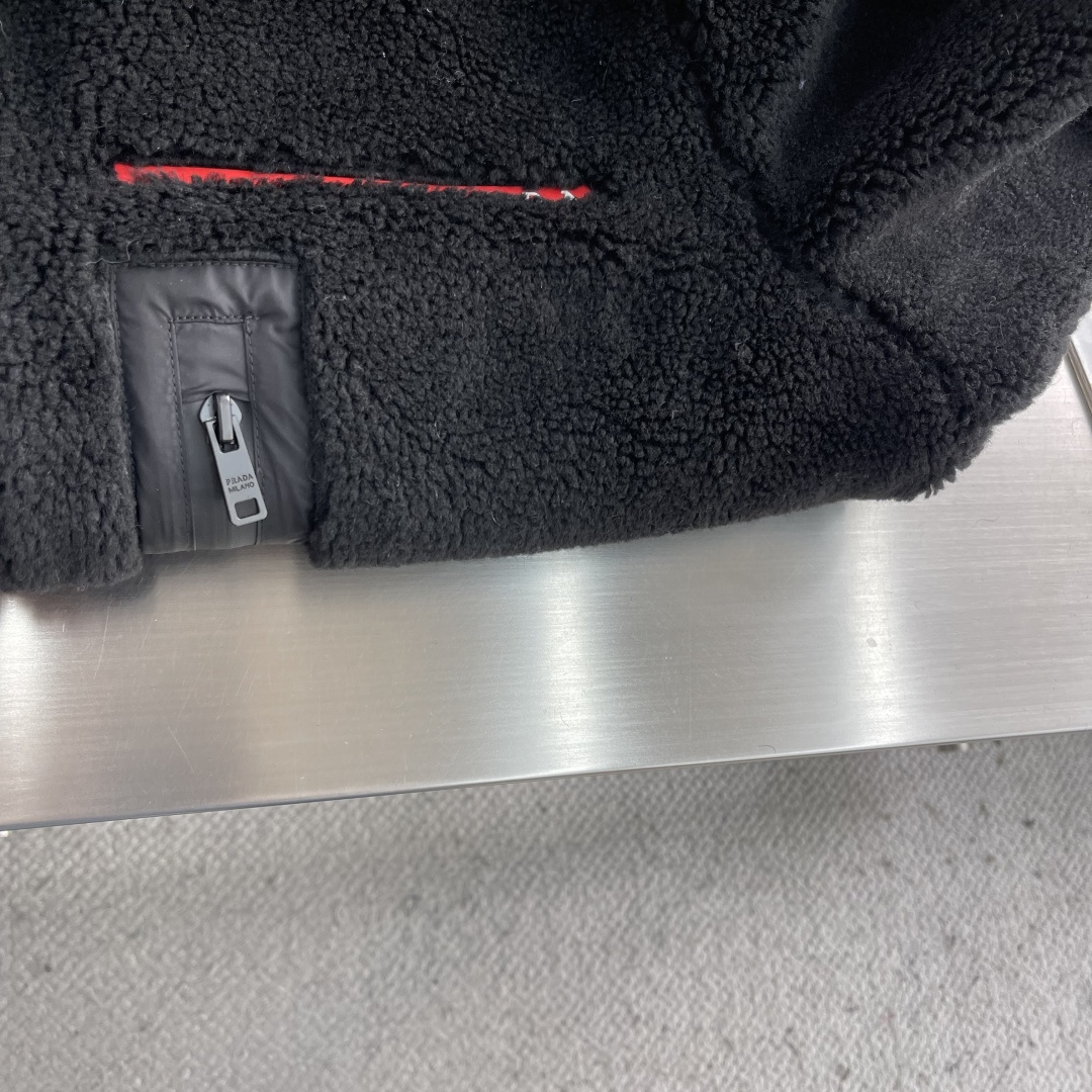 -PRAD 新款双面穿连帽夹克。这款夹克采用摇粒绒与防风面料拼接设计，兼具保暖性与机能感。胸前红色品牌标