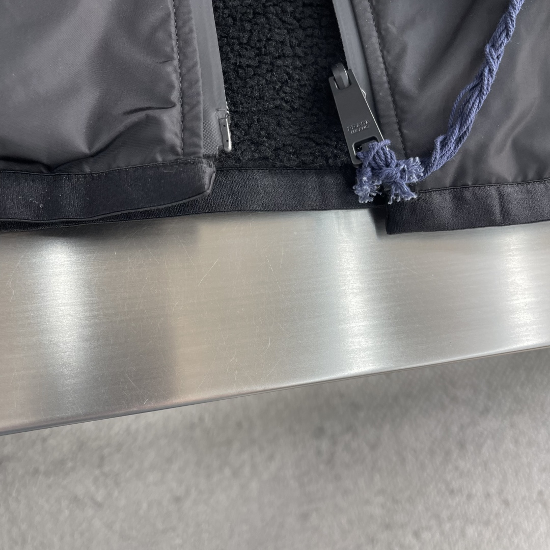 -PRAD 新款双面穿连帽夹克。这款夹克采用摇粒绒与防风面料拼接设计，兼具保暖性与机能感。胸前红色品牌标