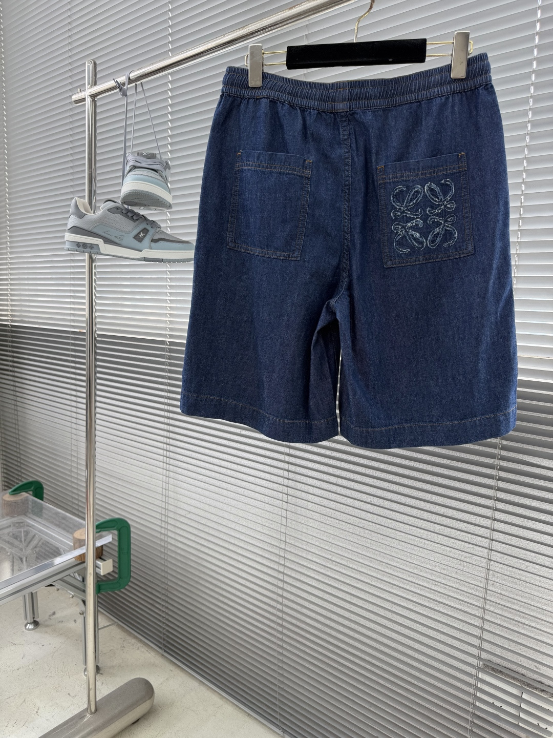 NO:955140,Shorts - LOEW patch pocket embroidered denim shorts are made of lightweight cotton chambray denim fabric and are made with plain weave and close weaving technology. The warp and weft cotton yarns are evenly intertwined. The fabric surface presents a delicate and clear denim grain texture, which is soft and thin to the touch. At the same time, it has a moderate drape, is stiff and not easy to wrinkle and deform. The gray fabric is washed, pre-shrunk and softened to remove the hard starchy feel of the fabric, making the upper body light and pressure-free, breathable and perspiration-wicking without stuffing the crotch.  The Anagram pattern is created using an exclusive appliqué process. First, the cut denim pattern pieces are accurately positioned on the patch bag base, and fixed on the positioning frame of the embroidery machine to prevent deviation. The needle is double-layered and densely embroidered to lock the fabric pieces along the outer contour of the pattern, and special special  The raw edge embroidery stitch method outlines the edge, and the embroidery threads are staggered and stacked to create a fluffy and three-dimensional tassel texture. The multi-layer lock embroidery structure firmly fixes the patch and is not easy to warp and peel off. The tassel texture is full and three-dimensional. After manual refinement, the lines are clean and neat, with both three-dimensional visual texture and solid firmness.  1. The waistband is sewn with widened double-layer panels, built-in high-elastic elastic bands, and multiple parallel top-stitched lines are evenly locked to prevent loosening and curling deformation. It is paired with a drawstring made of the same fabric, reinforced with metal eyelets and perforated, and the cord is threaded and locked tightly. The waistline can be adjusted freely, and the elasticity transition is natural, so it does not constrict the waist after being worn for a long time.  2. The overall cut of the trousers body is simple and neat, with long double-line open stitching on the side seams and the inner crotch. All splicing corners and stress points on the crotch bottom are all knotted to eliminate the problem of thread breakage and tearing during long-term activities. The contrasting color topstitch is even and straight, the stitch length is uniform, the cut edges are delicate, and there is no lint or burr inside, taking both beauty and structural stability into consideration. Size 46 48 50 52 Size pants long-sitting waist 46  54 106 78 48 55 11082 50 56 11486 52 5711890,,loewe,shorts,19860909短裤 -LOEW 贴袋绣花牛仔短裤 选用轻盈棉质青年布牛仔面料,采用平纹紧密梭织工艺打造,经纬棉纱均匀交织,布面呈现细腻清晰的牛仔颗粒肌理,触感柔软轻薄,同时其自带适度垂坠感,挺括不易起皱变形.坯布经水洗预缩软化处理,去除布料硬性浆感,上身轻盈无压,透气排汗不闷裆. 采用专属贴布绣工艺打造Anagram纹样,先将裁剪成型的牛仔布图案裁片精准对位铺置在贴袋基底上,固定于绣花机定位框防止走位偏移.针头沿图案外轮廓双层密绣锁固布片,同步运用特殊毛边绣针法勾勒边缘,绣线交错堆叠塑造蓬松立体的流苏肌理,多层锁绣结构牢牢固定贴布,不易翘边脱片,流苏纹理层次饱满立体,手工精修后线条干净利落,兼具立体视觉质感与扎实的牢固度. 1、腰头采用加宽双层裁片复合缝制,内置高弹松紧带,多道平行明线均匀锁缝,拉扯不易松垮、卷边变形.搭配同面料抽绳,金属气眼加固穿孔,绳带走线锁边密实,可自由调节腰围,松紧过渡自然,久穿不勒腰. 2、裤身整体裁片简洁利落,侧缝、内裆通长双道明线缝制,所有拼接转角、裆底受力点全部加做打枣套结,杜绝长期活动断线、撕裂问题.撞色明线均匀顺直,针距统一,裁片锁边细腻,内里无毛絮毛刺,兼顾美观与结构稳定性. 码数46 48 50 52 尺码裤长坐围腰围 46 54 106 78  48 55 11082 50 56 11486  52 5711890,,loewe,shorts,,Men's clothing