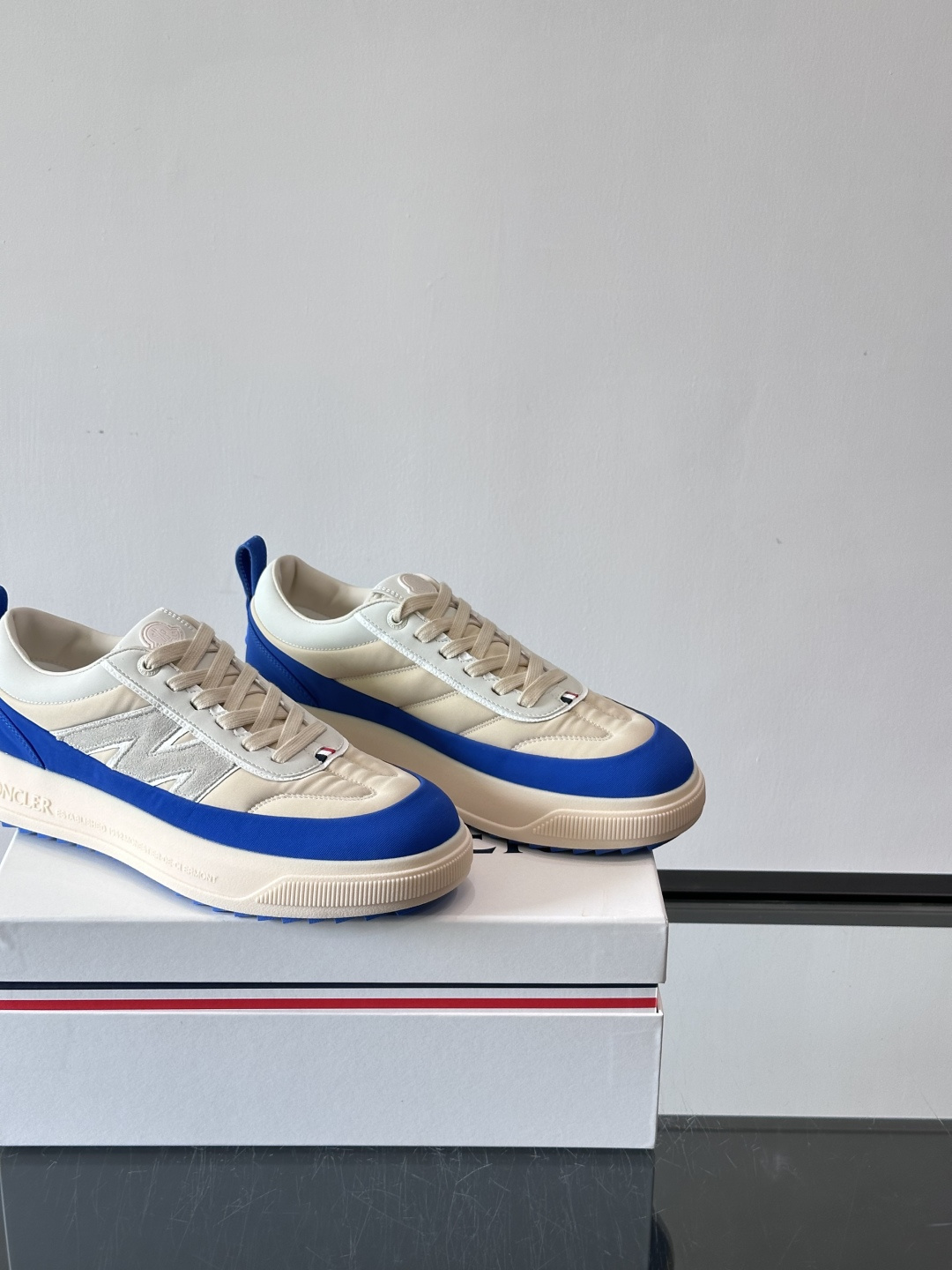 Moncler这款休闲运动鞋，主打简约百搭风，鞋面拼接米白+浅灰，蓝色橡胶鞋底和侧边点缀超有活力。鞋舌和